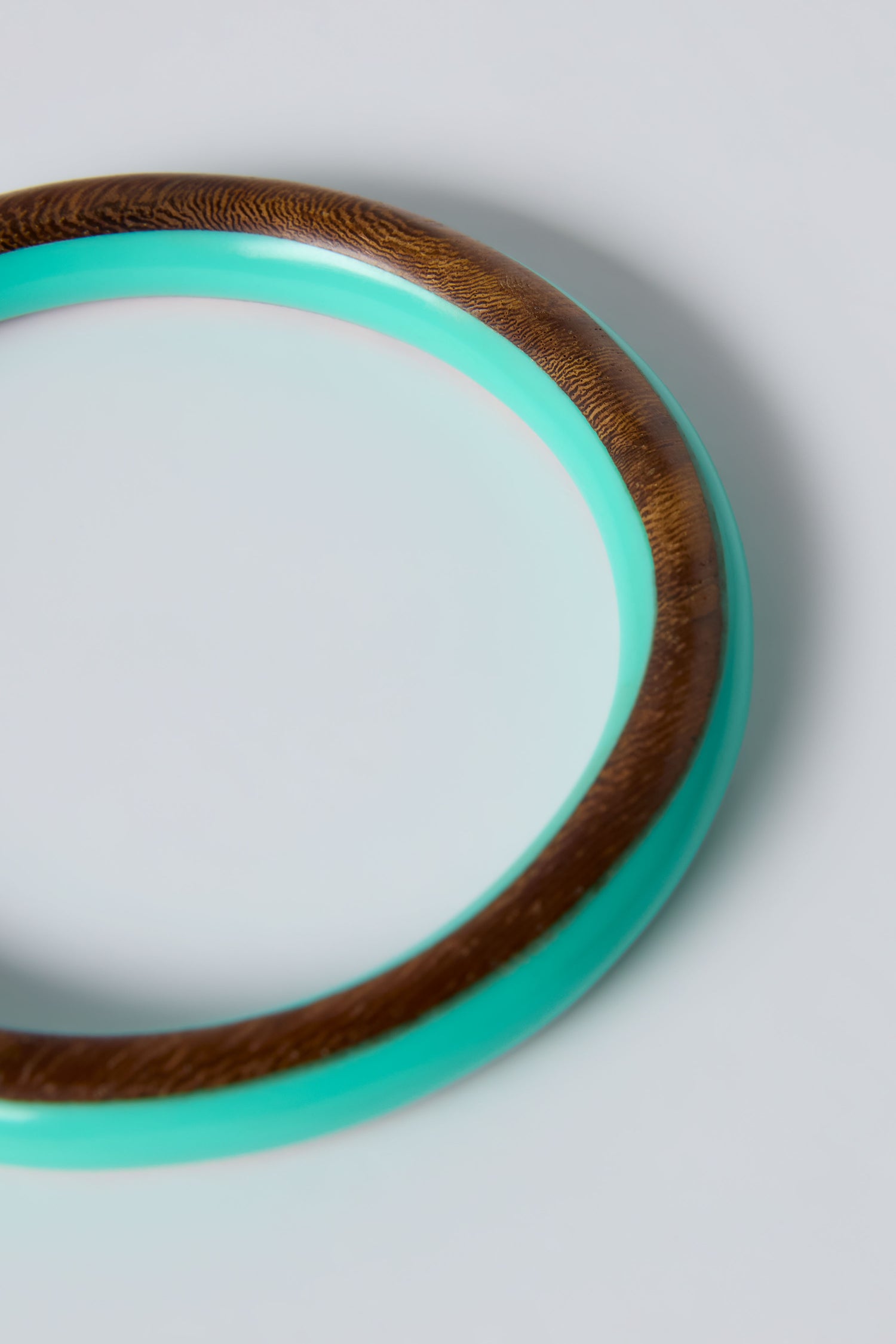 A close-up of the Cosmos Turquoise Wooden Bangle, featuring a teal outer ring and brown inner section, displayed on a light gray background—ideal for showcasing summer jewelry in the style of Ernesto de Barcelona.