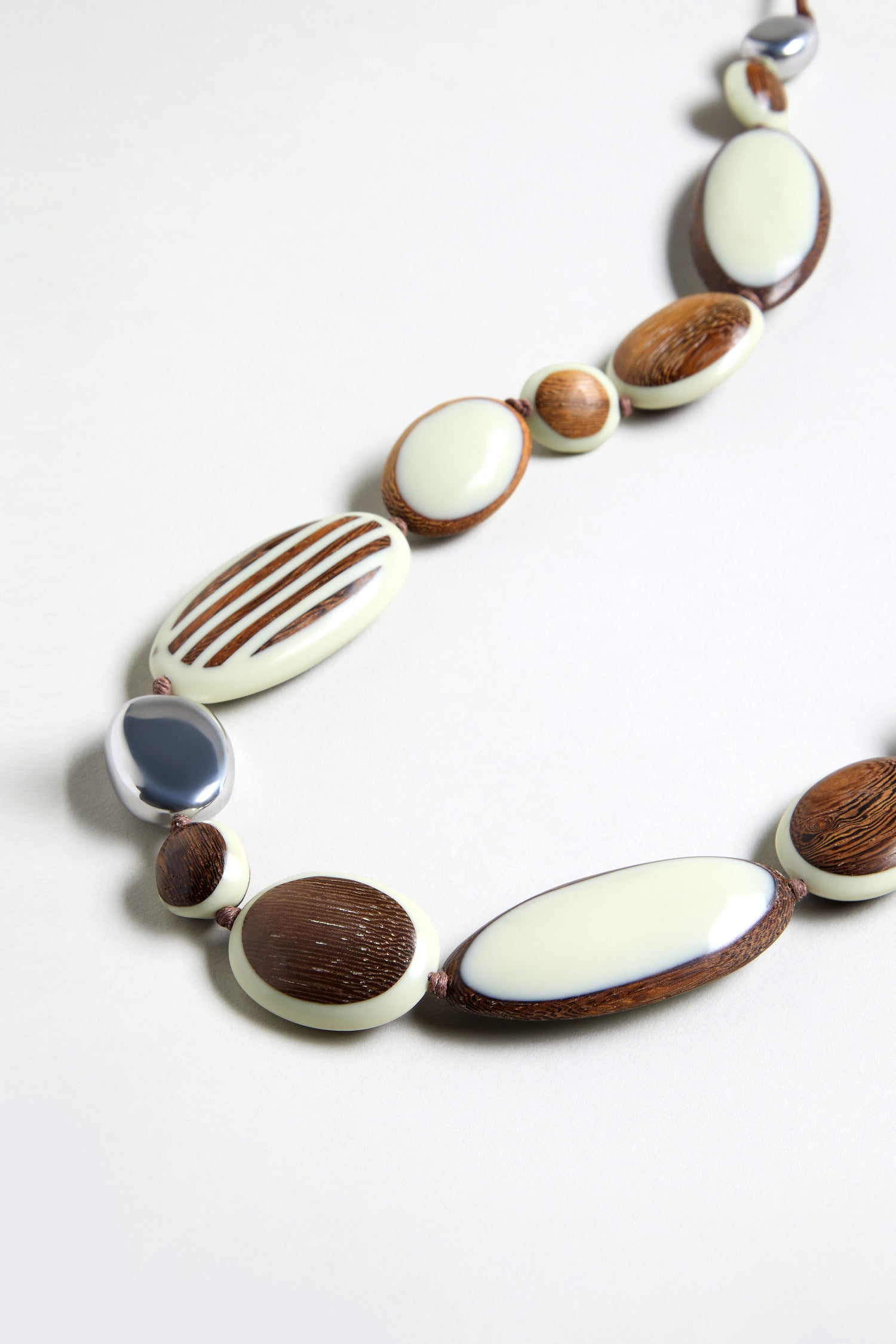 The Humbug Necklace showcases oval and round beads in cream, brown, and silver hues, made from natural wood and recycled aluminium.