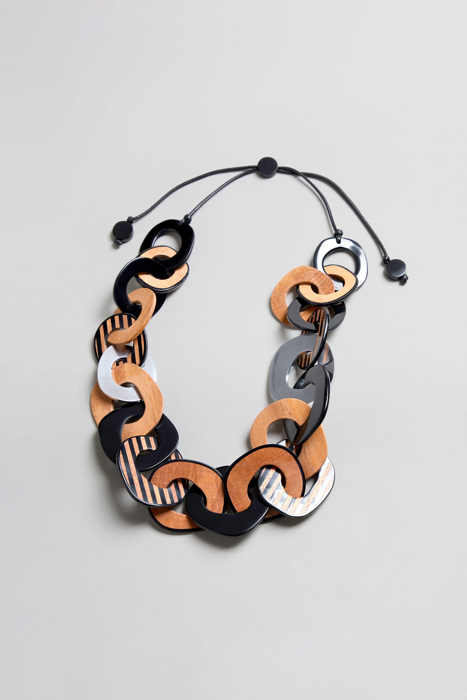 Introducing the Black Stripe Wooden Resin Links Necklace—a bold statement collar featuring oversized interlocking resin and wood links in black, brown, and gray tones, finished with a black adjustable cord and sliding knots.