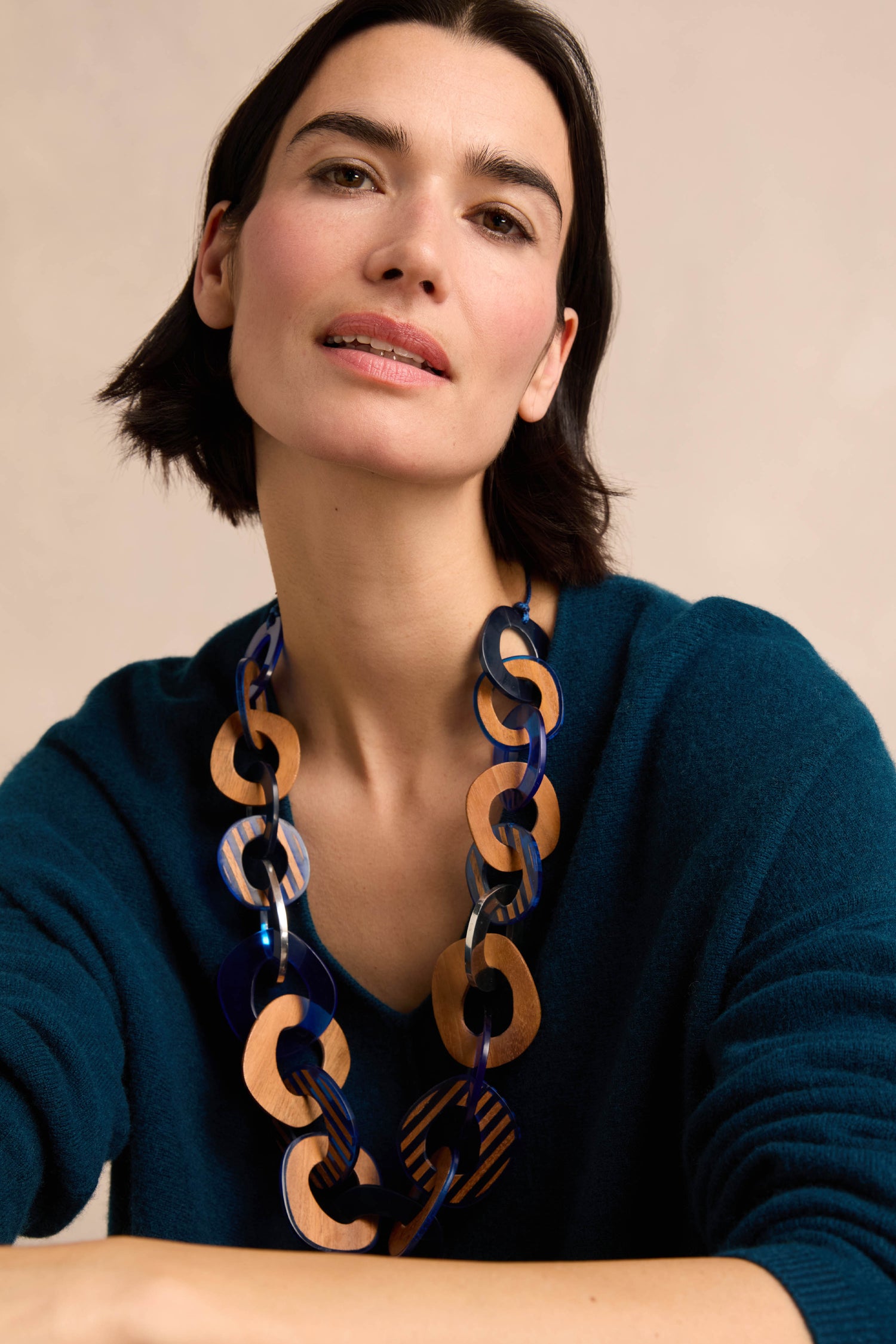A woman with short dark hair, wearing a teal sweater and the Blue Stripe Wooden Resin Links Necklace, poses against a neutral background.