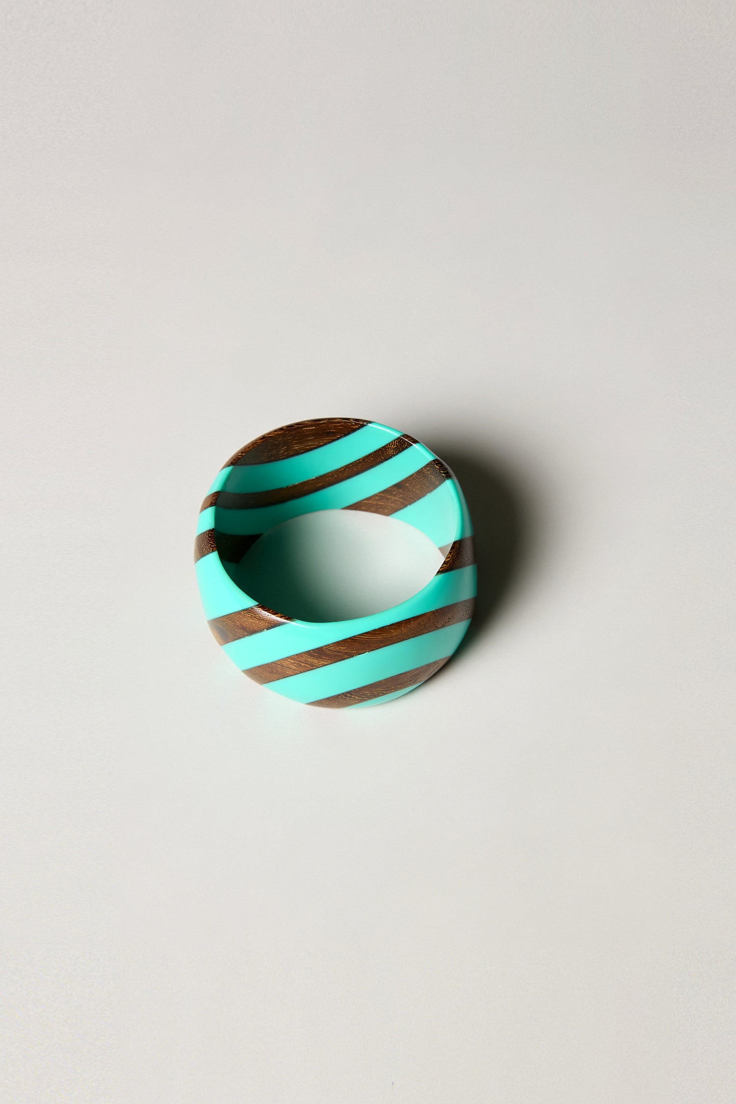 Handmade in Barcelona, the Turquoise Wooden Stripe Bangle showcases bold turquoise and brown diagonal stripes set in turquoise resin on a round wooden bracelet, displayed against a plain light background.