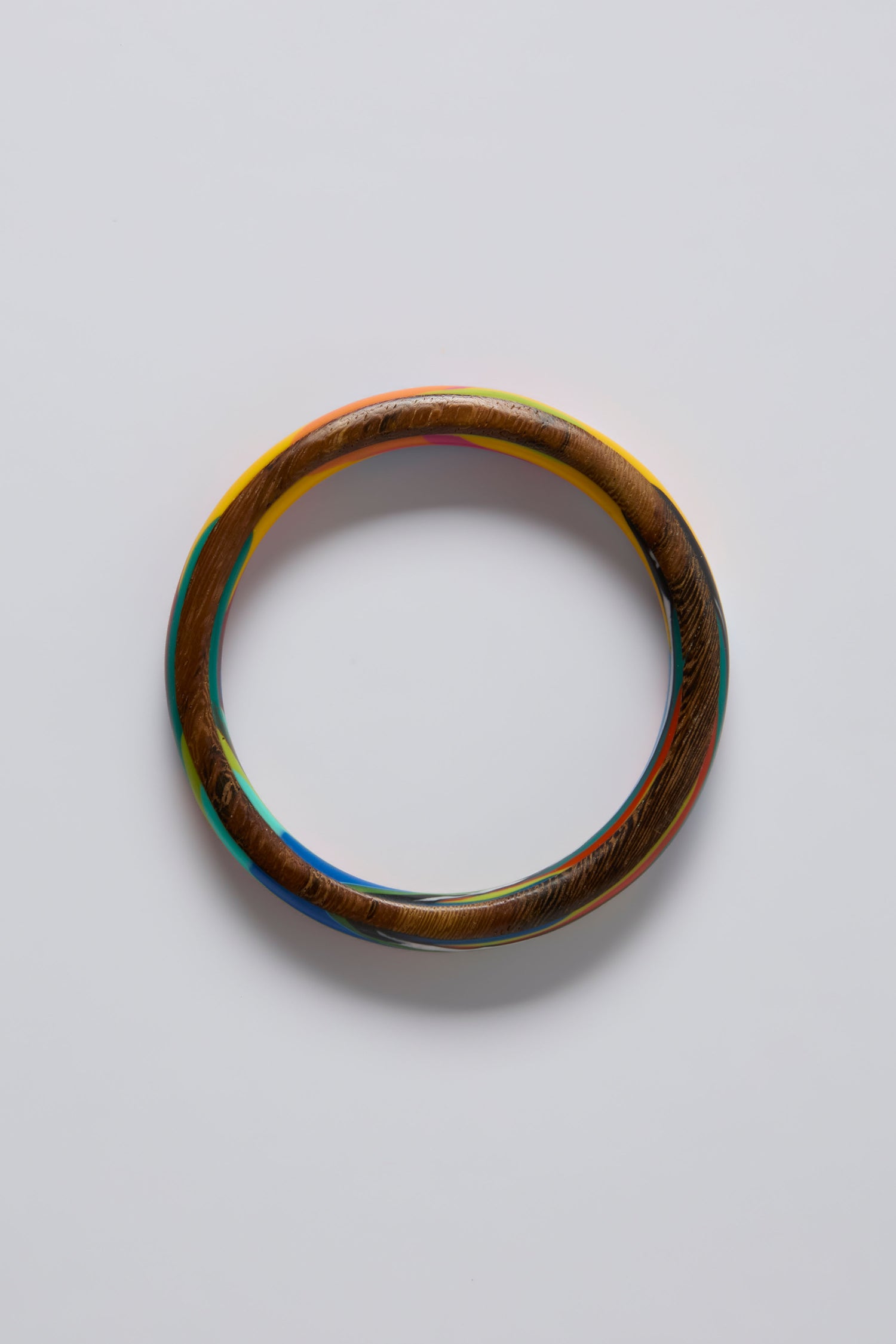 The Flores Rainbow Bangle, featuring a sculptural design and polished wood with a smooth finish, is displayed on a plain white background.