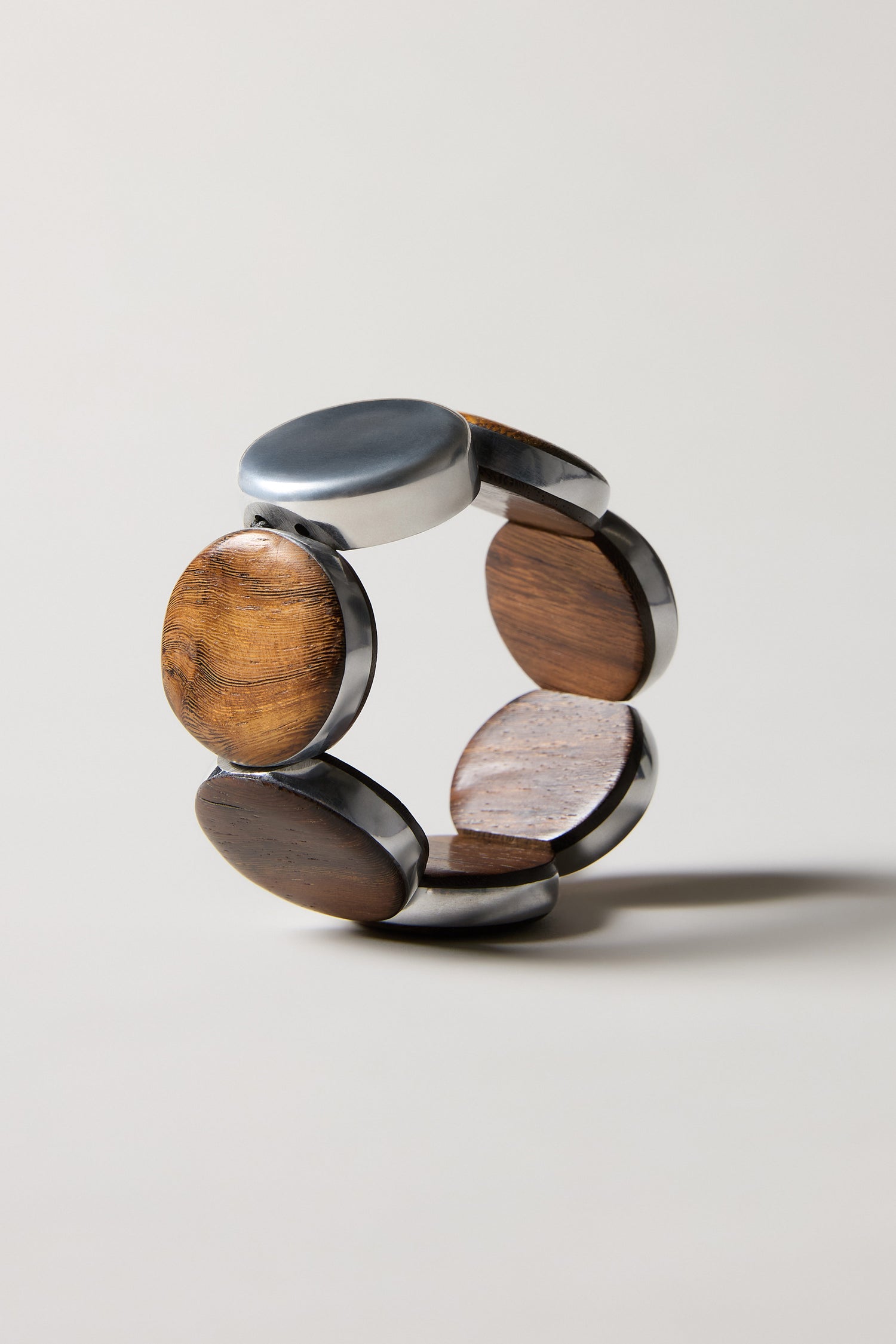 The Silver Wooden Spheres Bracelet features alternating silver and wood segments in a circular pattern, highlighting exquisite handmade Spanish jewelry against a light, neutral backdrop.