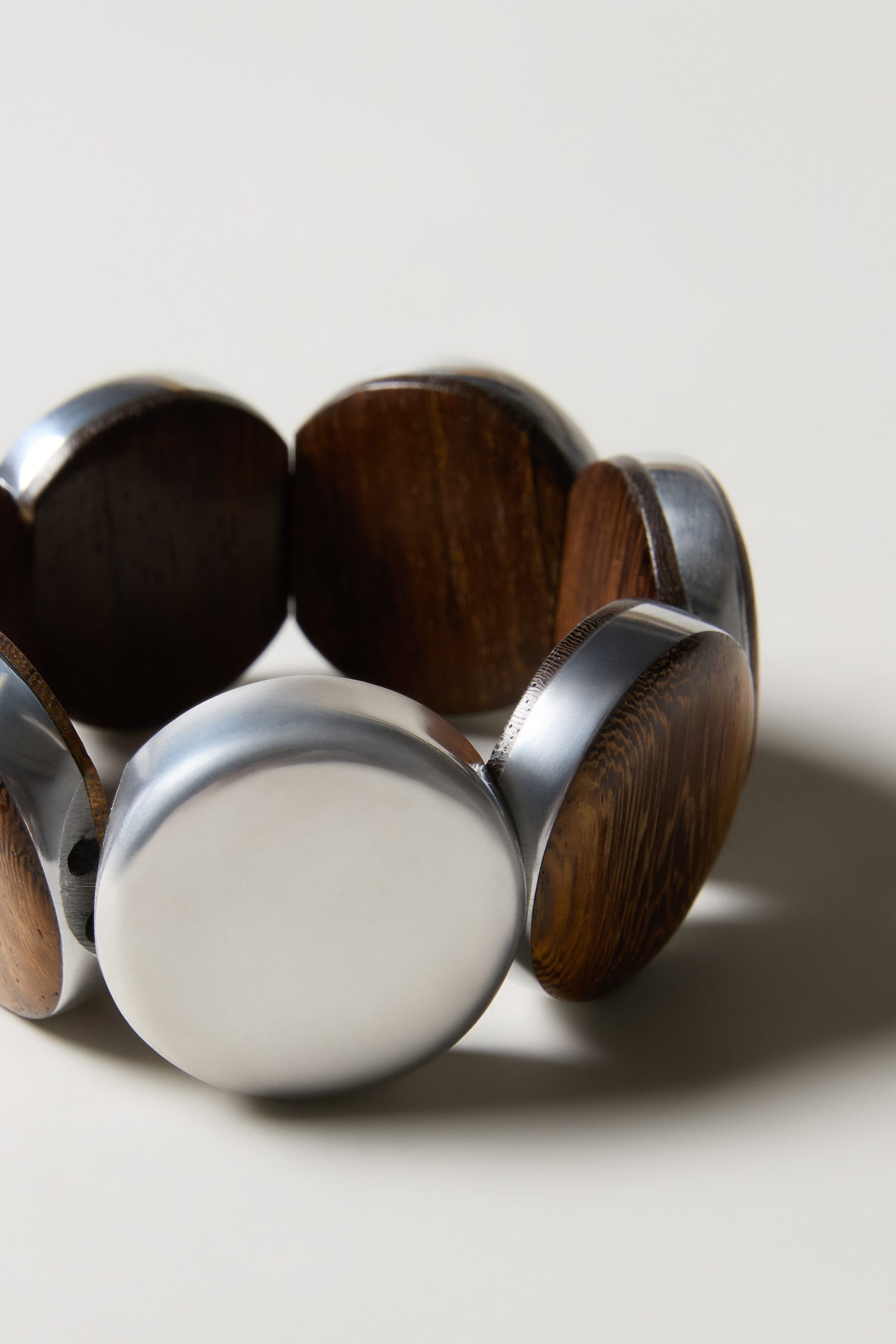 The Silver Wooden Spheres Bracelet features alternating polished metal and dark wood oval segments in a circular design, capturing the artisanal flair of handmade Spanish jewellery.