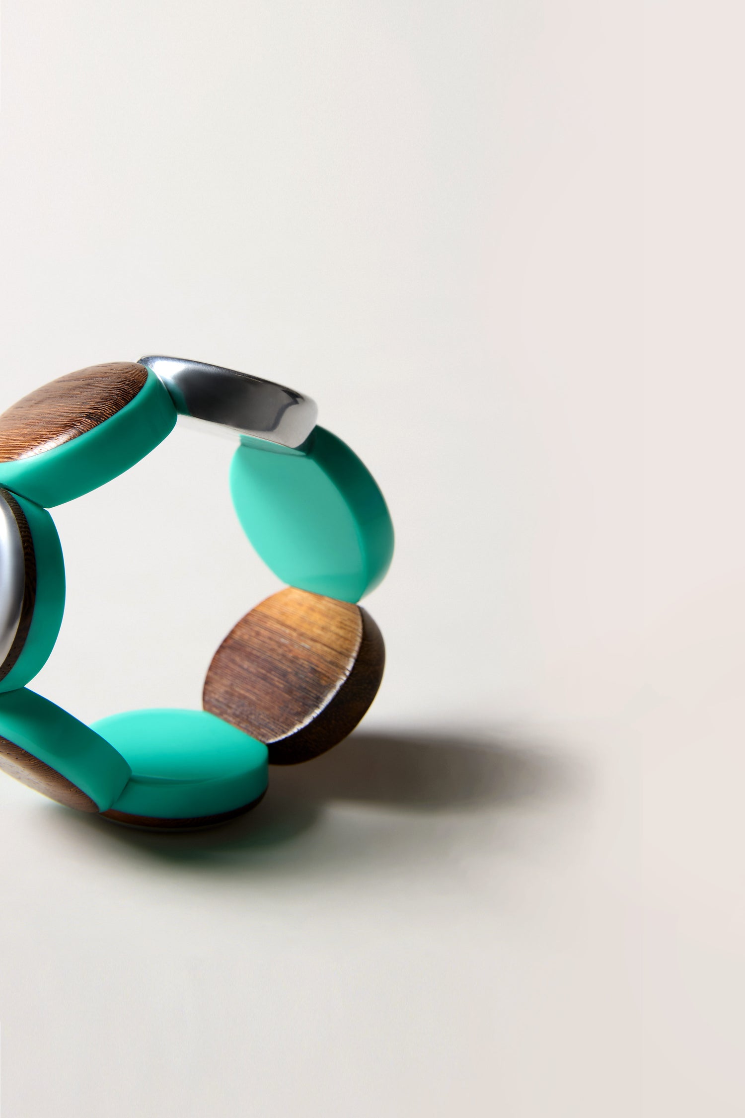 The Wooden Spheres Bracelet, with circular wooden, silver, and turquoise segments in teal and earthy tones, is shown on a light neutral background.
