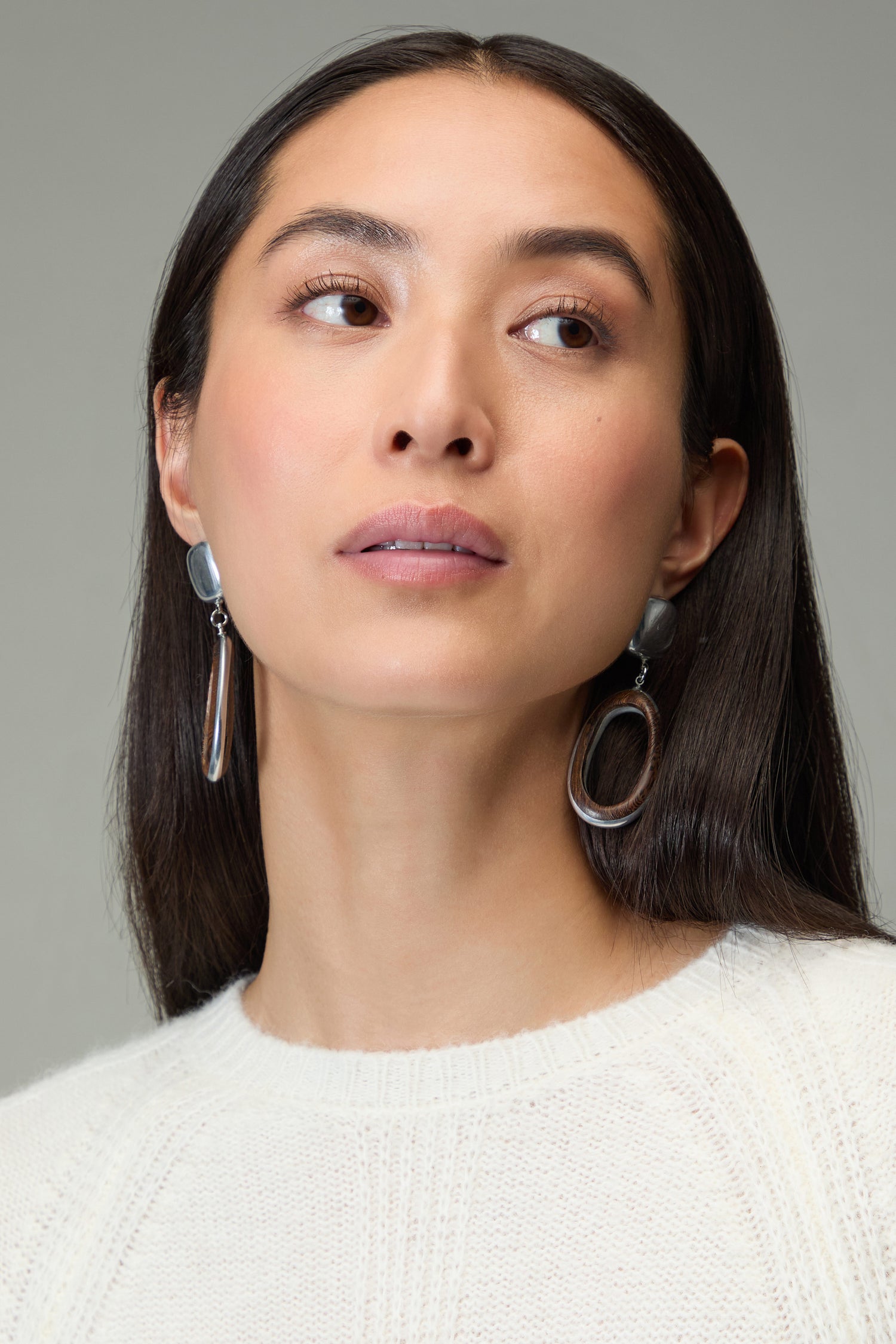 Woman with straight dark hair wears a white sweater and Wooden Silver Clip-On Earrings, looking slightly to the side against a neutral background.