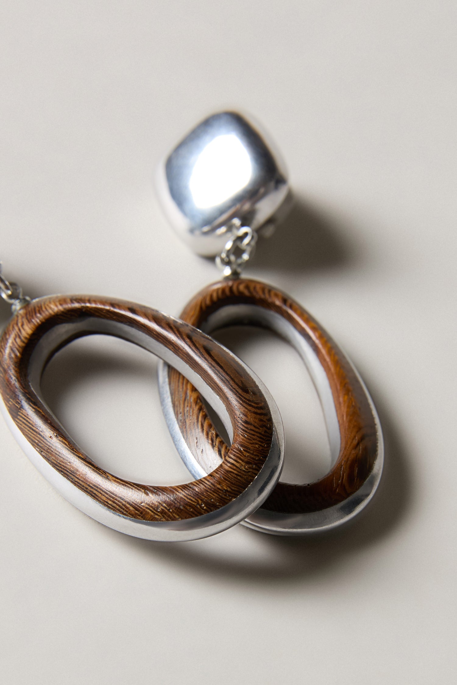 A close-up of the Wooden Silver Clip-On Earrings, handcrafted in Spain, featuring sculptural oval wooden and silver loops attached to a square silver stud.