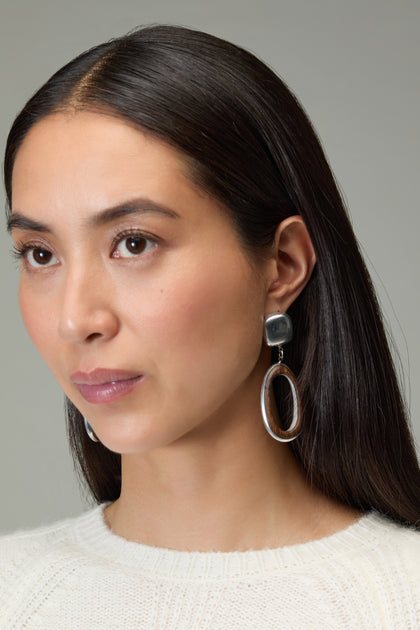 A woman with long dark hair wears a cream sweater and Wooden Silver Clip-On Earrings, looking slightly to the side against a plain background.