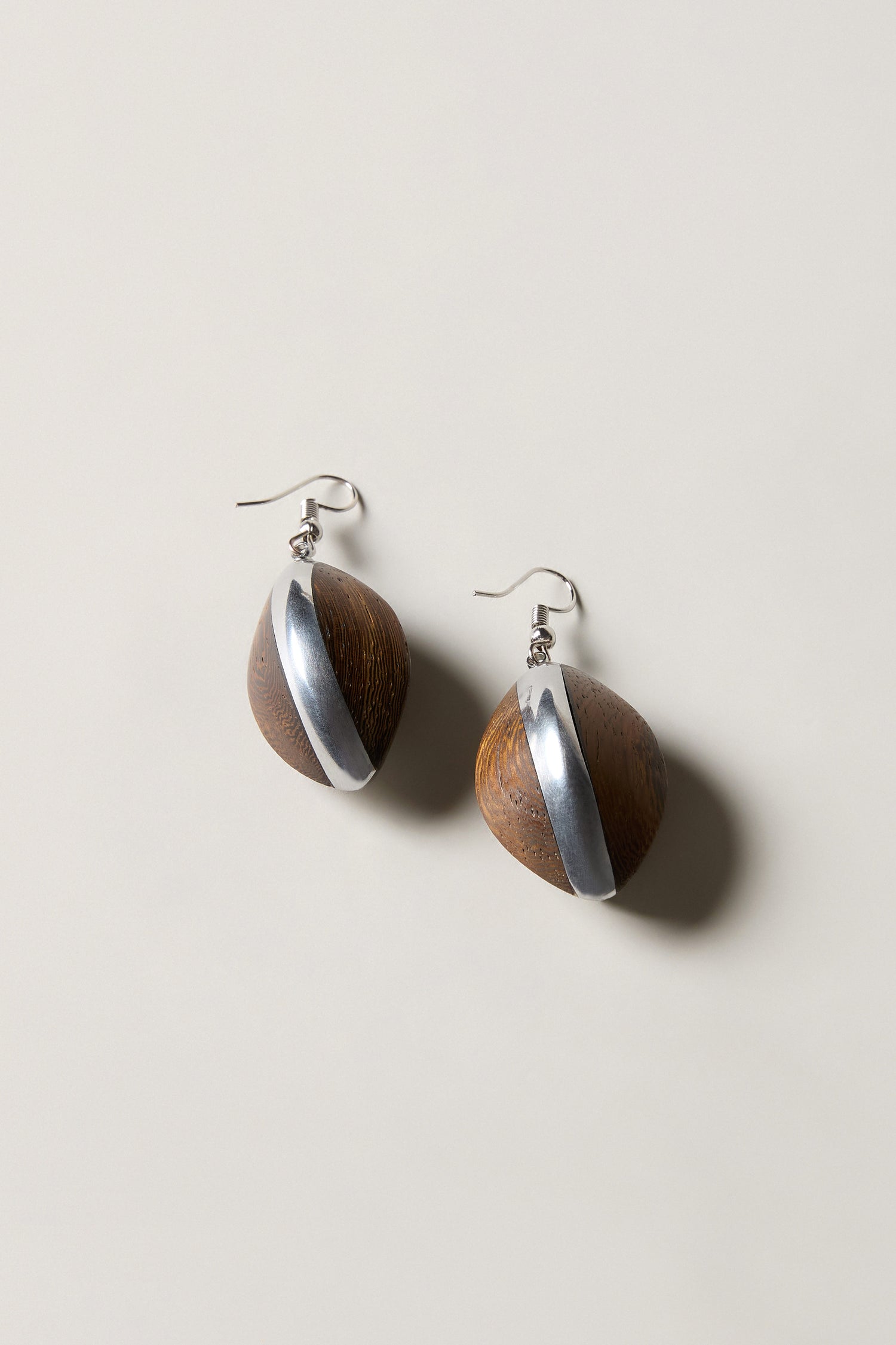 Wooden Oval Pebble Earrings featuring handcrafted oval wooden beads with diagonal silver stripes and silver hooks, elegantly displayed on a light background.