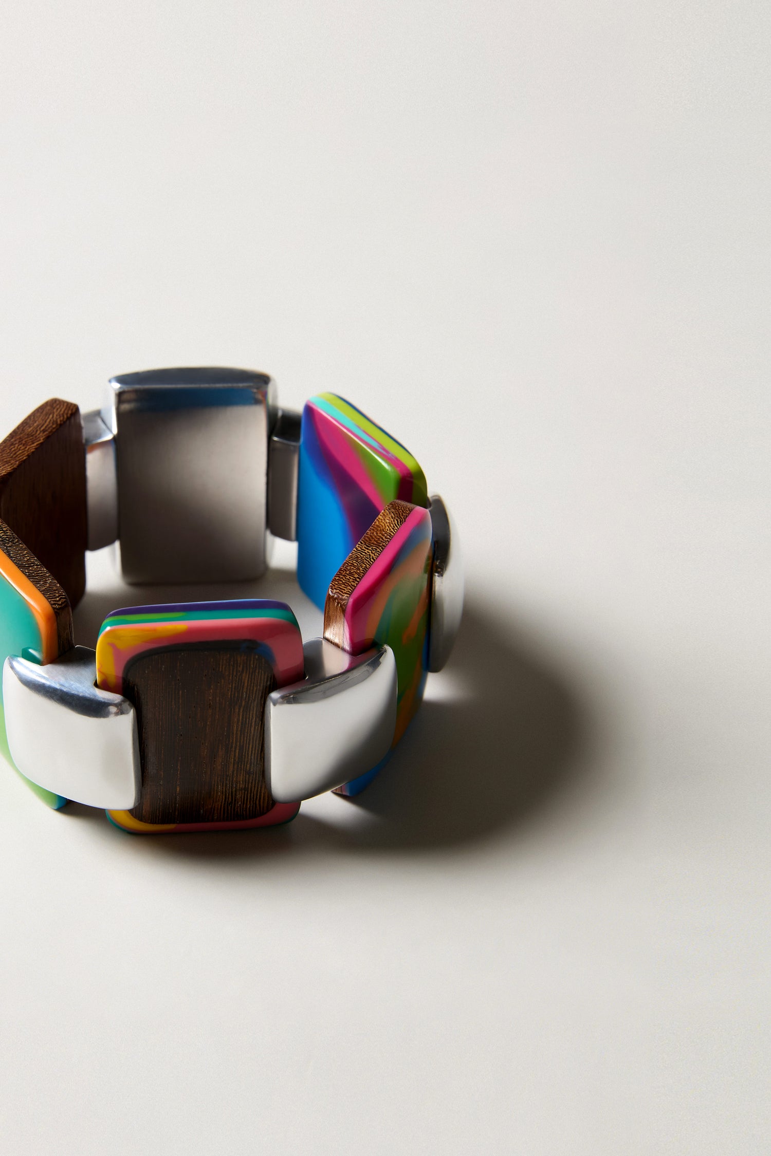 The Colourburst Squares Links Bracelet is a chunky, handcrafted accessory with alternating marbled resin, metal, and wood-like rectangles in a circular pattern, inspired by Barcelona’s vibrant design.