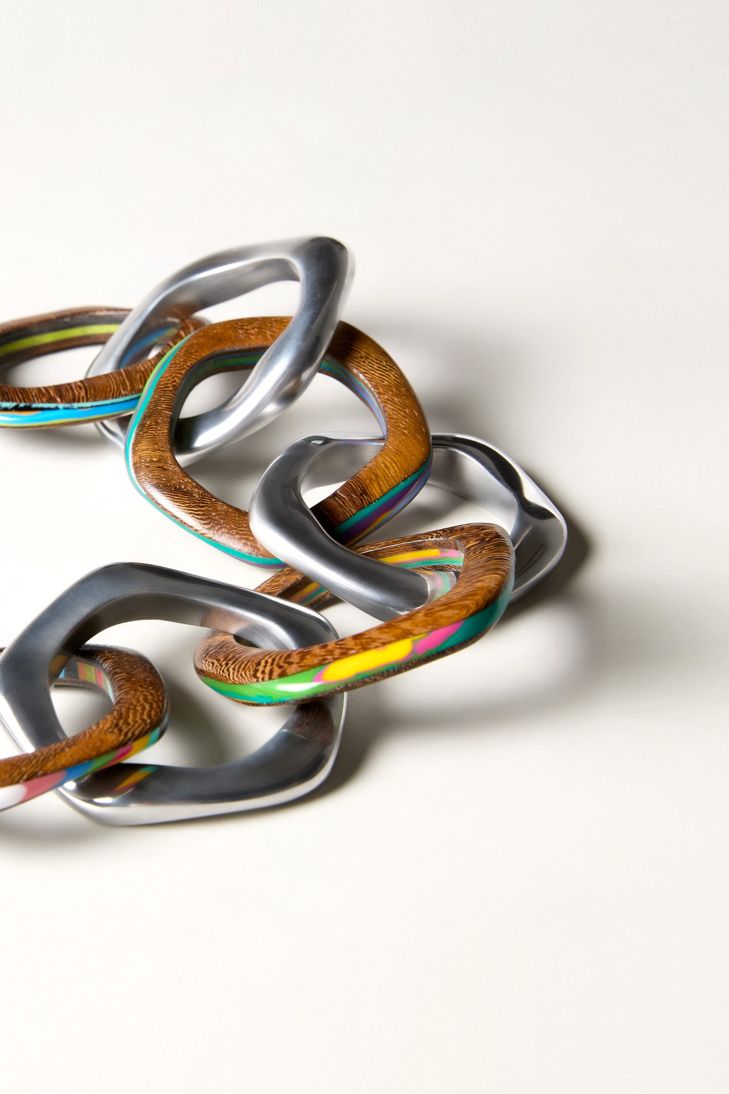 A close-up of the Olympus Links Necklace shows interlocking chain links of shiny metal and marbled resin, creating a striking geometric jewelry piece against a plain background.