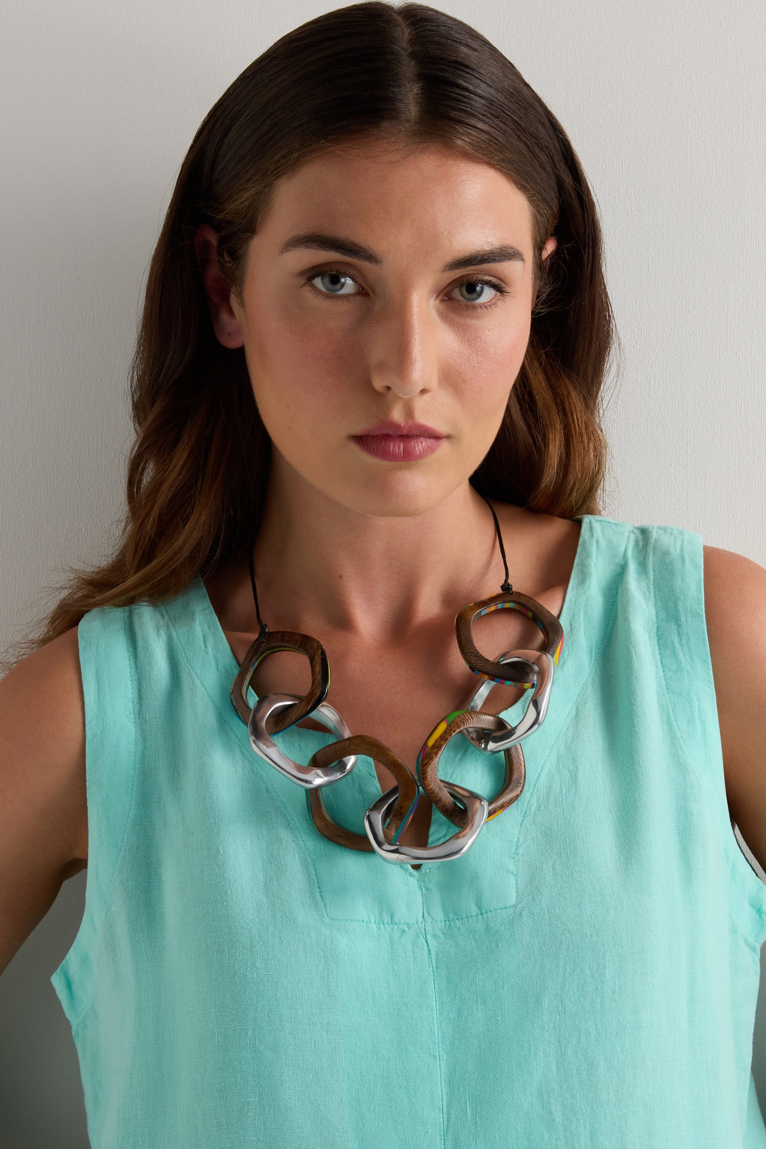 A woman wears the Olympus Links Necklace with a sleeveless light turquoise top, standing against a plain light background.