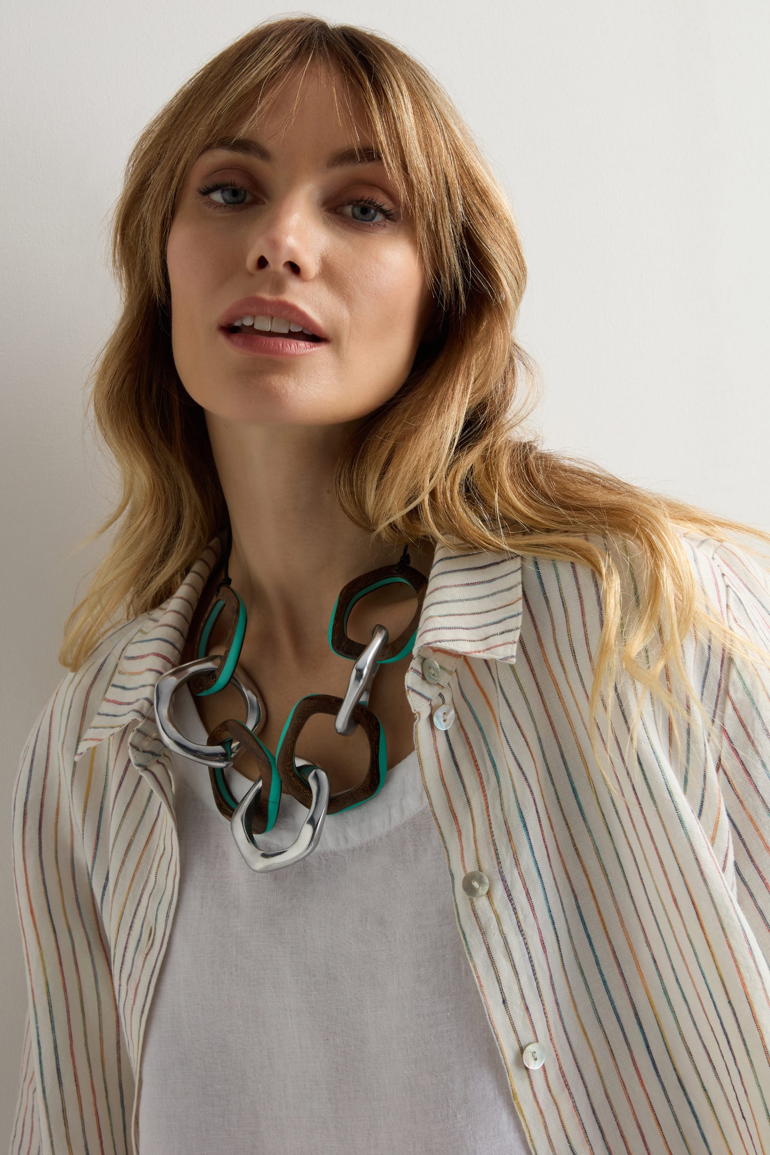 Woman wearing a white shirt with colorful stripes and a Turquoise Olympus Links Necklace, standing against a plain light-colored background.