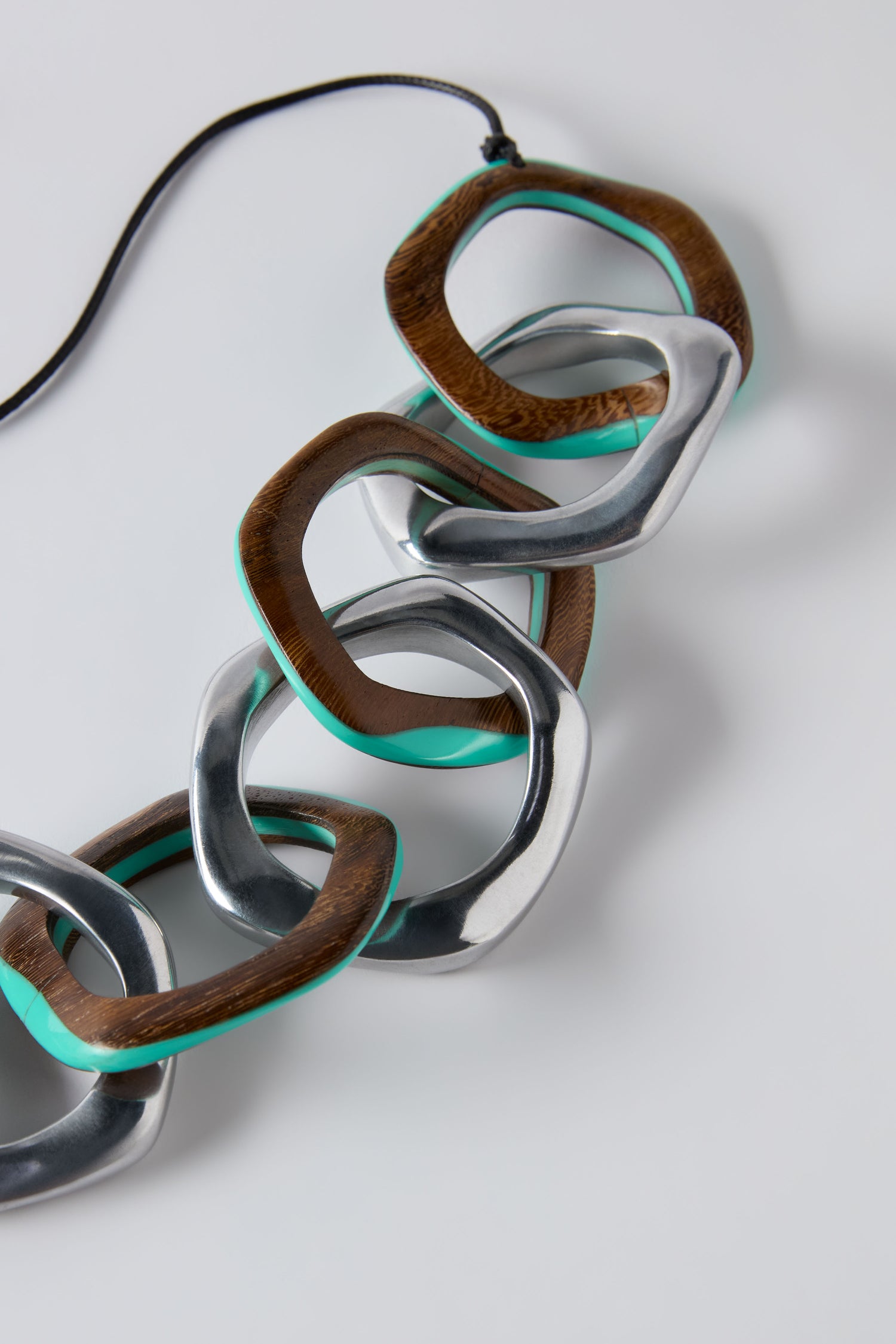 The Turquoise Olympus Links Necklace is a statement piece featuring oversized interlocking wood, silver metal, and turquoise links, showcased on a white background.