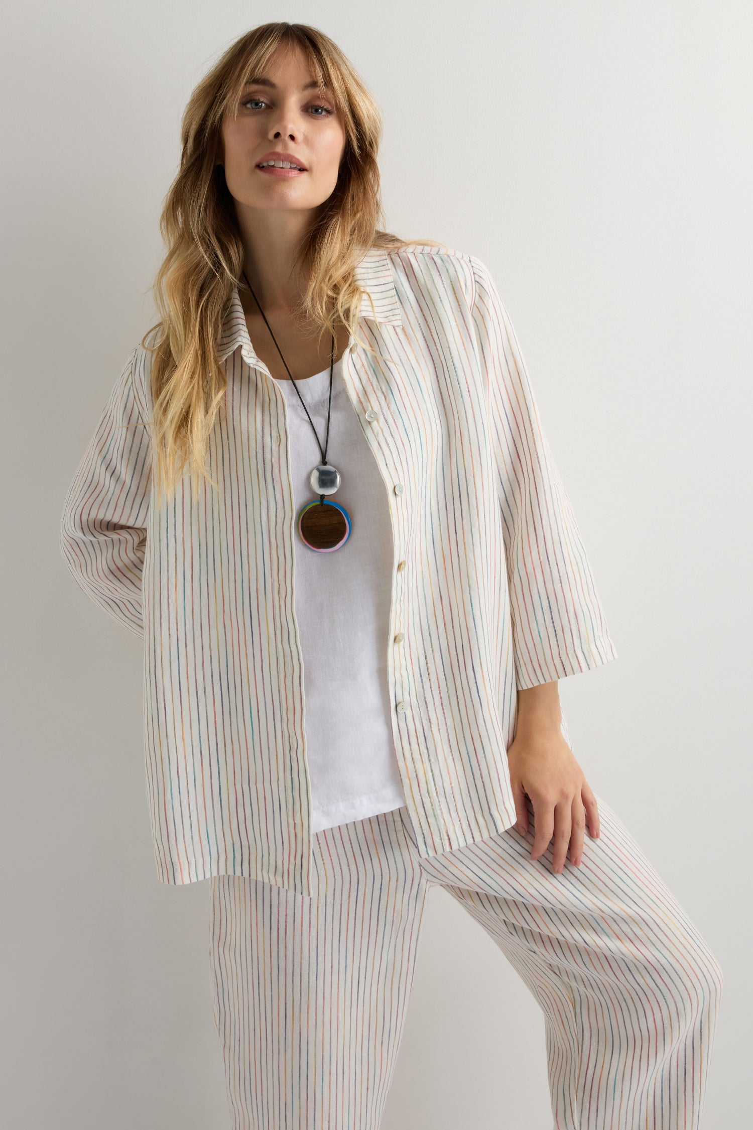 A woman in a light, striped pajama set over a white top wears the Colourburst Double Sphere Pendant necklace and stands against a plain white background.