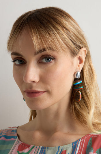 A woman with blonde hair wears Colourburst Wooden Pebble Earrings and a patterned top, looking at the camera against a plain background.
