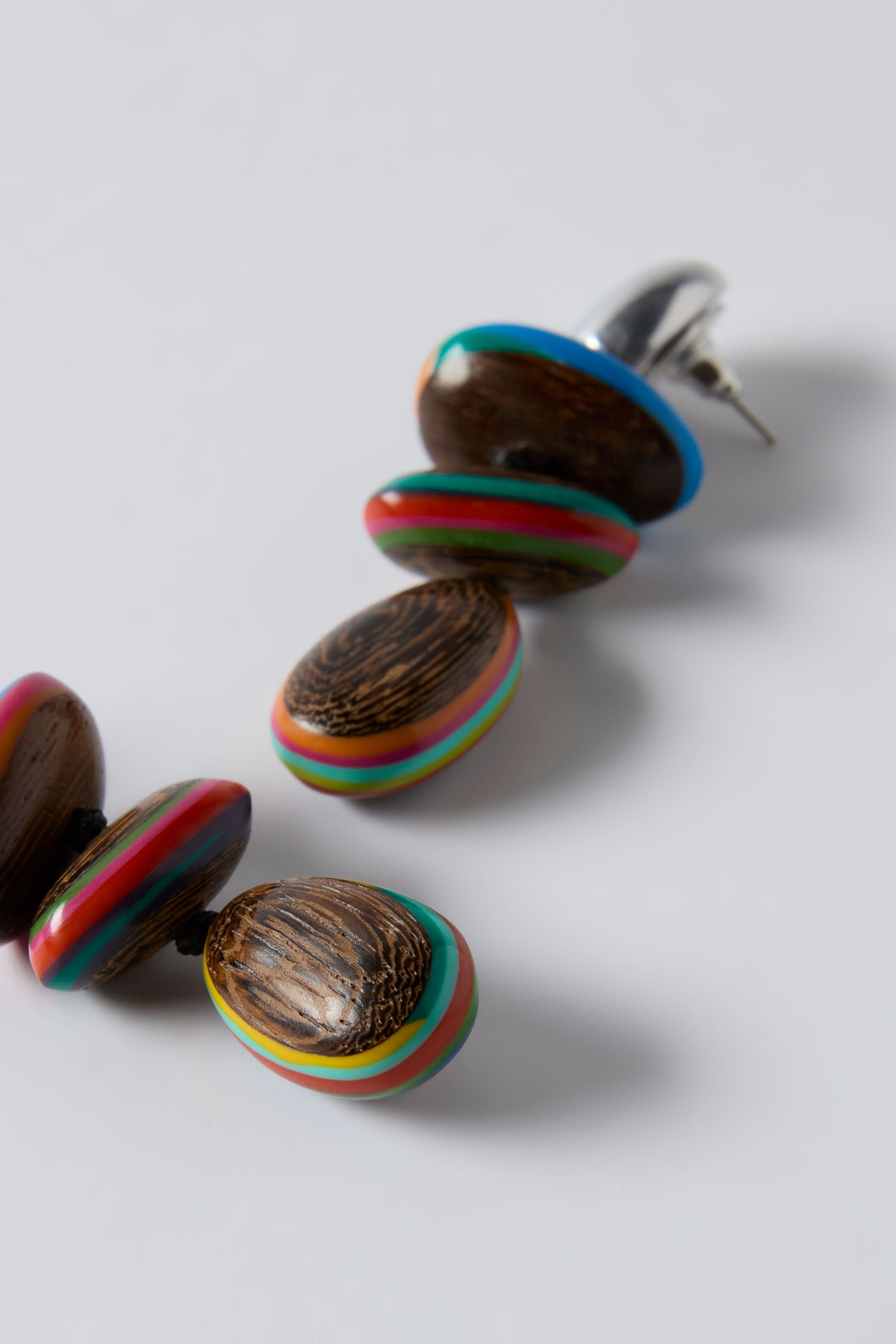 The Colourburst Wooden Pebble Earrings by Ernesto de Barcelona feature oval-shaped wooden beads with multicolored stripes, displayed on a plain white background.