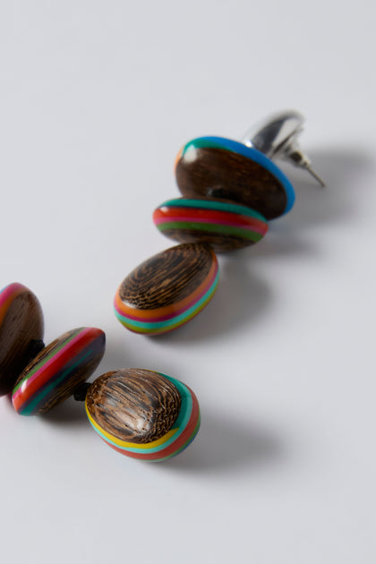 The Colourburst Wooden Pebble Earrings by Ernesto de Barcelona feature oval-shaped wooden beads with multicolored stripes, displayed on a plain white background.