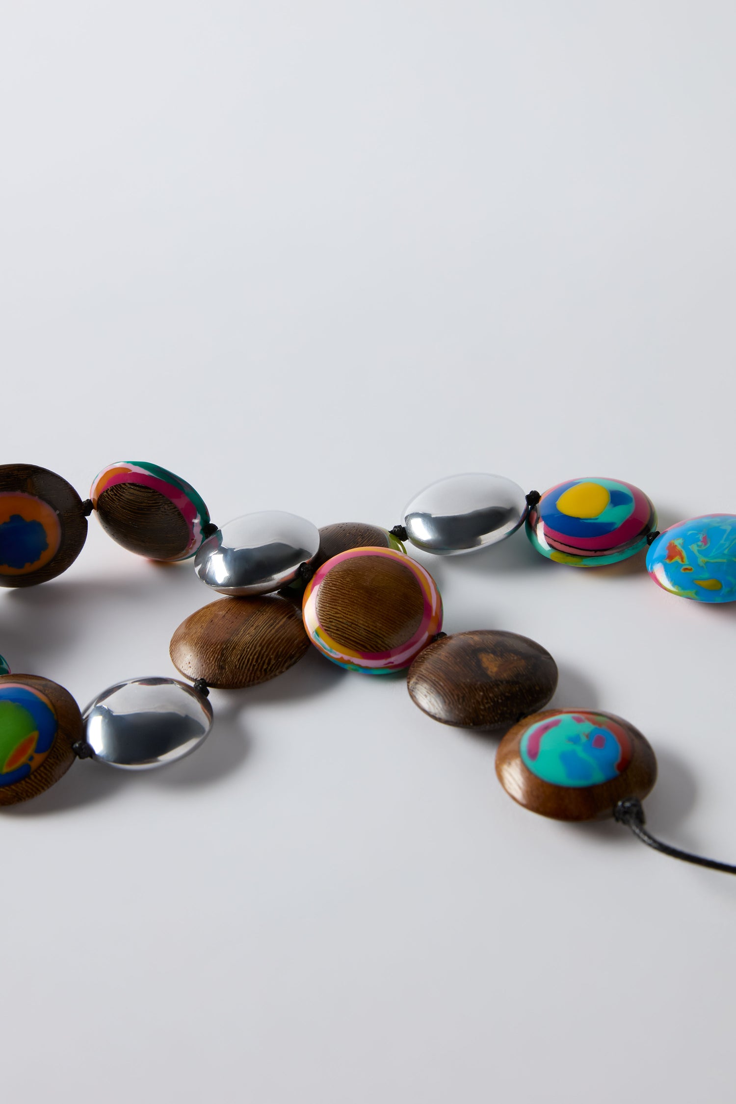 The Rainbow Riverstone Spheres Necklace by Ernesto de Barcelona features alternating round wooden, metallic silver, and colorful painted beads displayed on a white surface.