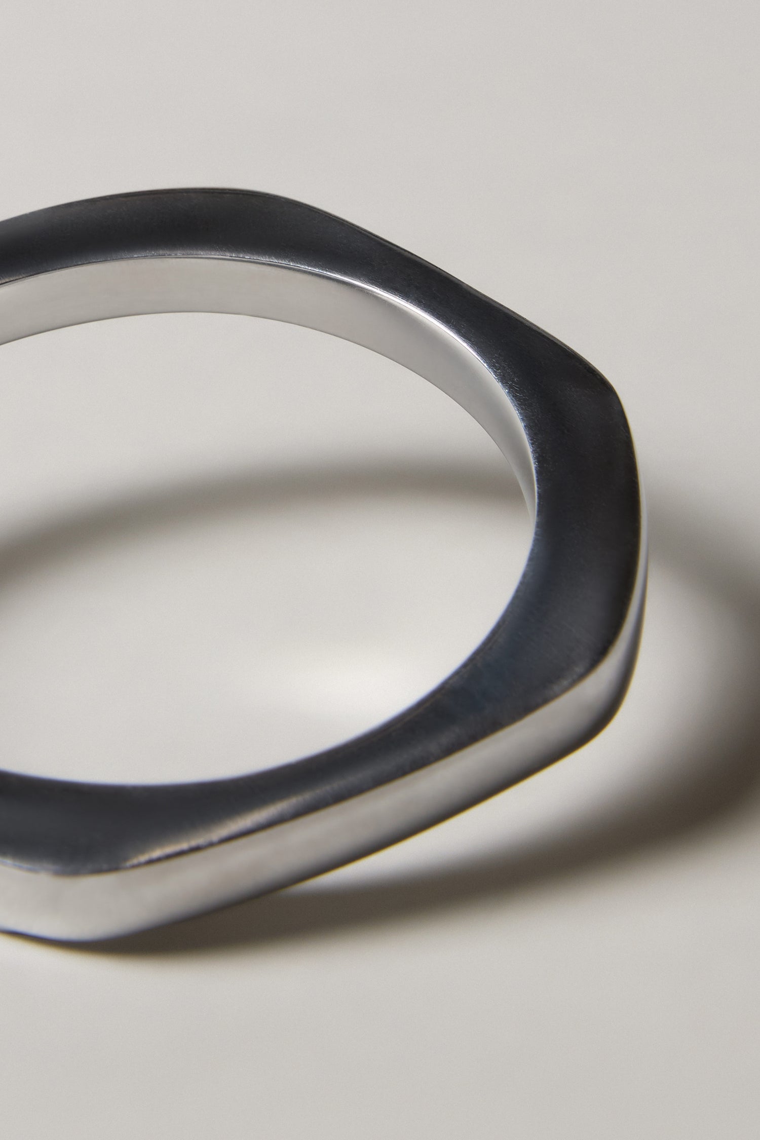 A close-up of the Solar Silver Bangle, a handmade Spanish jewelry piece with an irregular metallic shape, resting on a plain light surface.