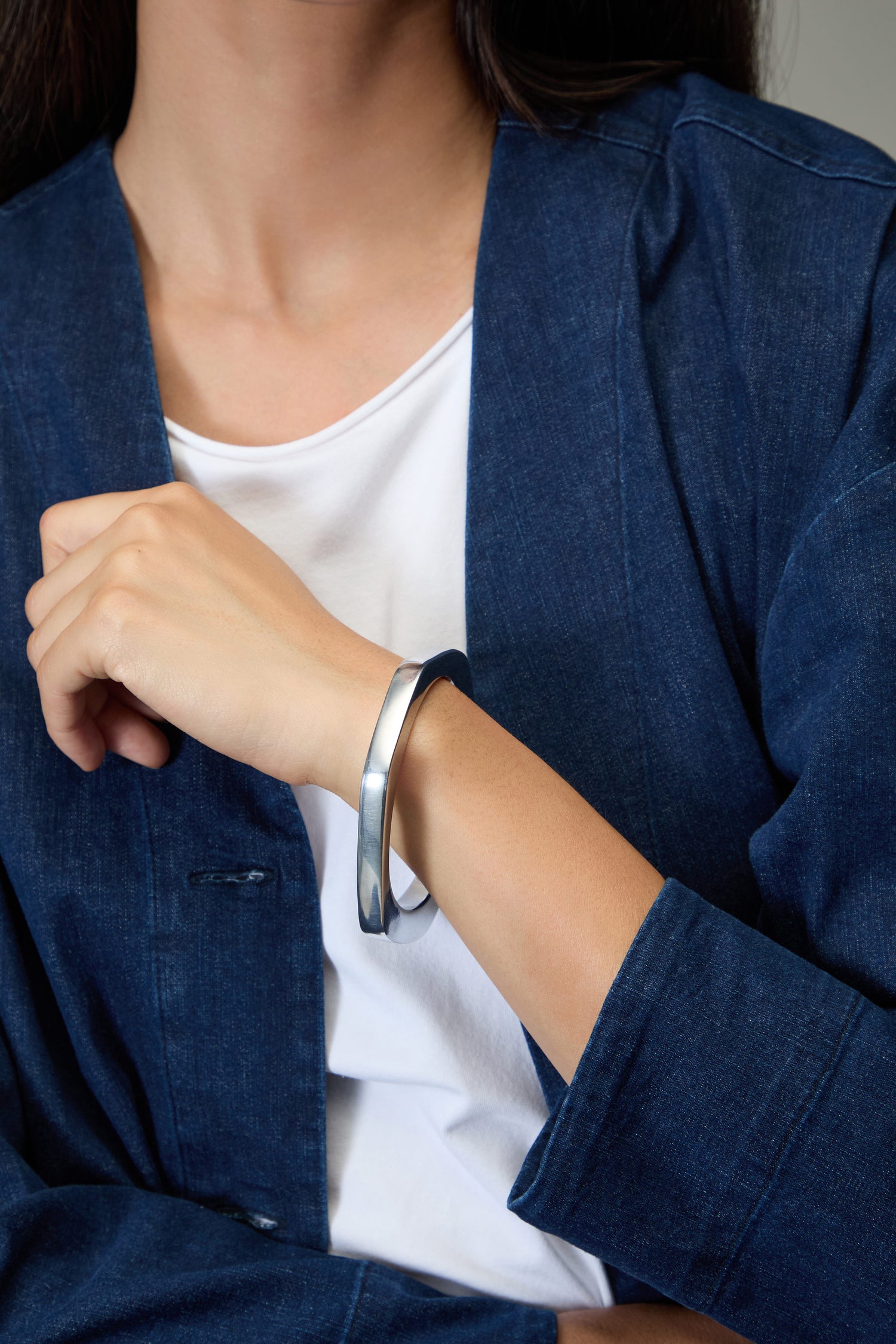 A person wearing a blue denim jacket and white shirt displays the Solar Silver Bangle on their wrist—a striking, minimalist piece of handmade Spanish jewelry.