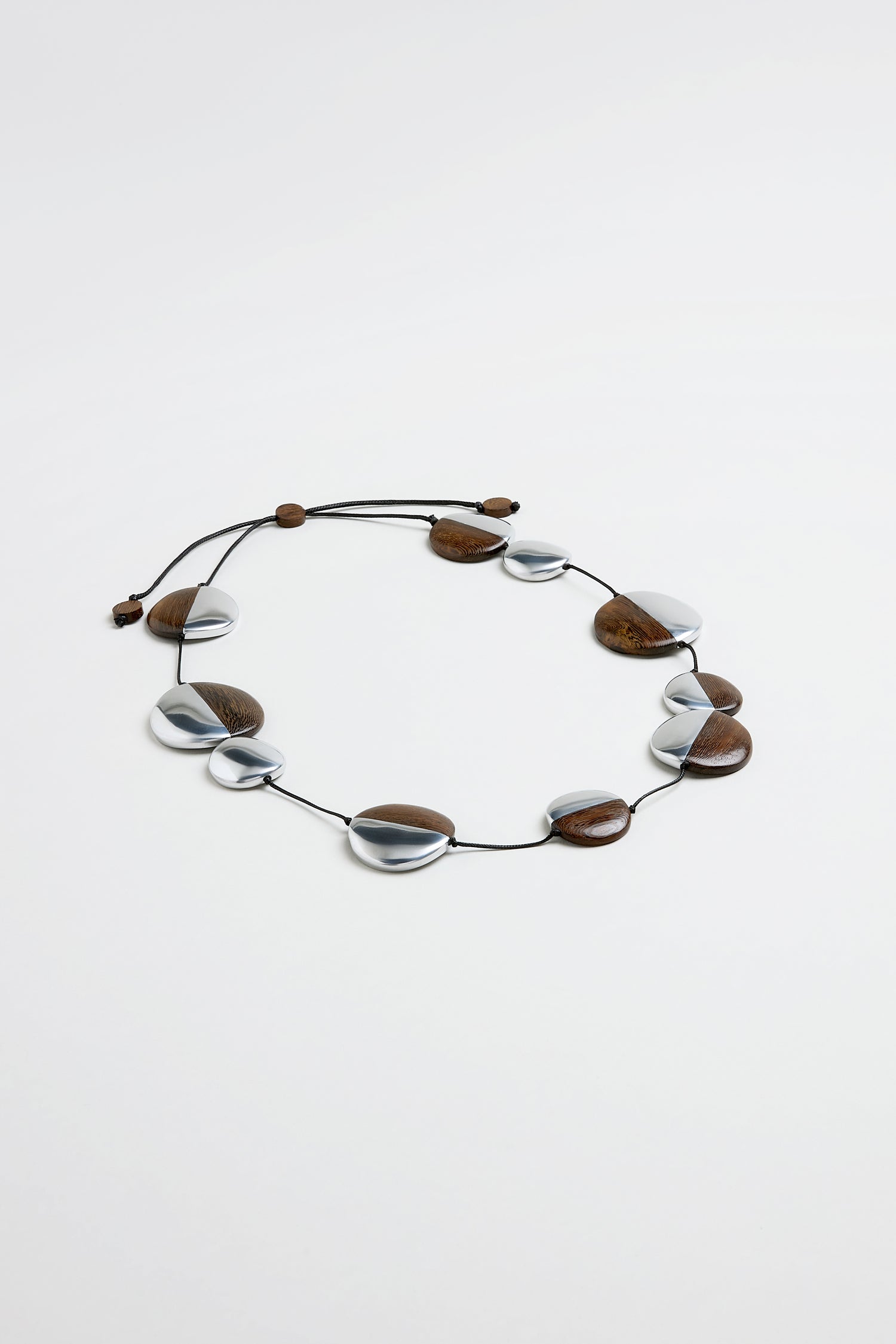 The Solar Spheres Necklace showcases alternating oval silver and brown wooden beads on a black cord with an adjustable sliding clasp.