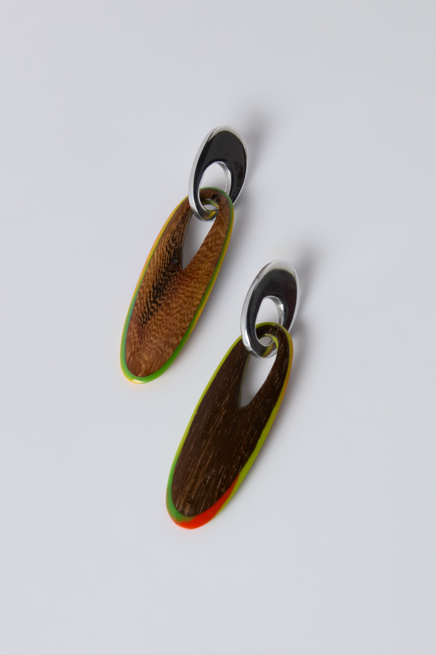 The Rainbow Wooden Oval Links Earrings feature sculptural drop design with silver tops and elongated wooden pendants accented in green and red, displayed on a plain white background.