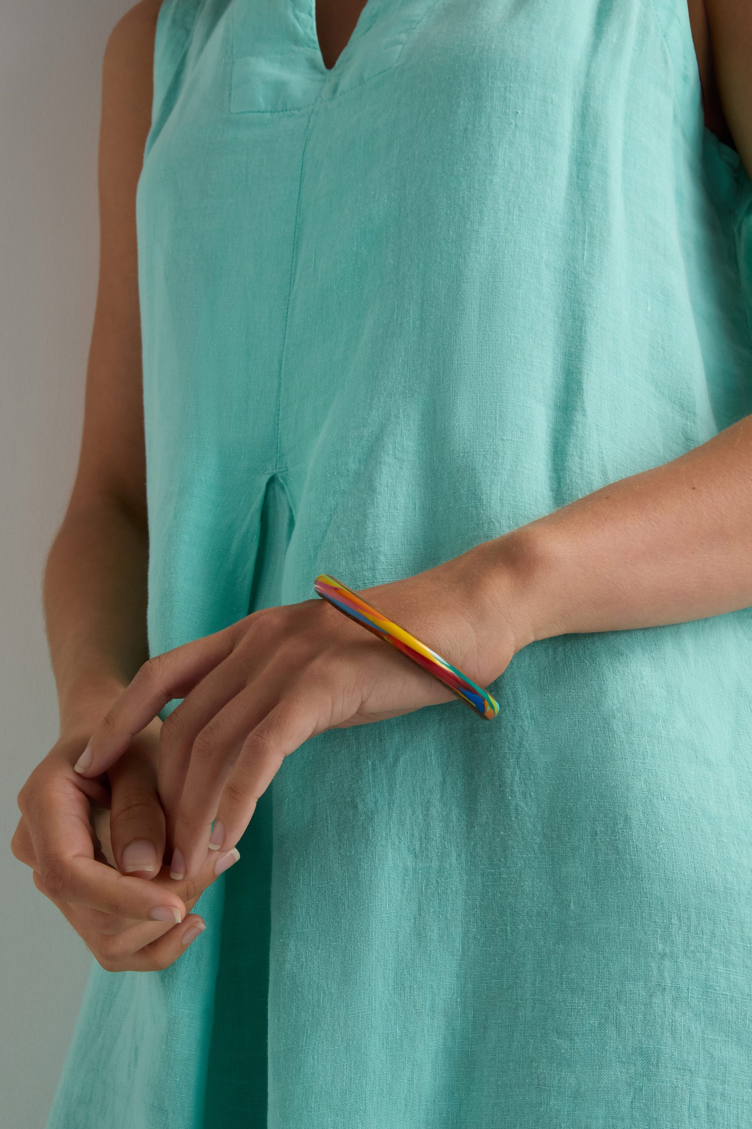 A person in a sleeveless light blue dress wears the Rainbow Marble Bangle, handmade in Barcelona, on their wrist with hands gently clasped together.