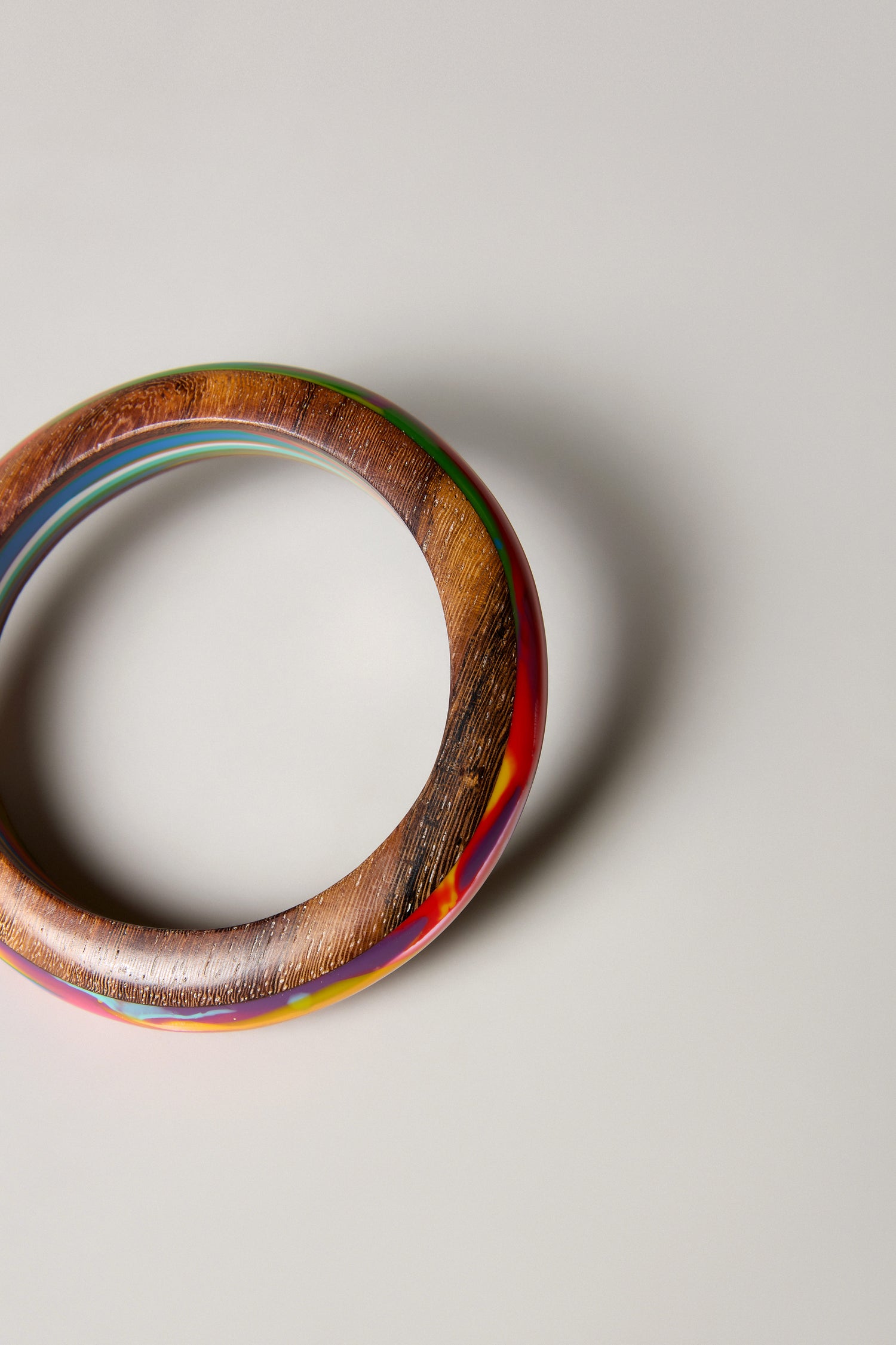 The Rainbow Marble Bangle, a handmade round bangle from Barcelona with a glossy, multicolored finish, rests on a light grey surface, partially visible in the upper left corner of the image.
