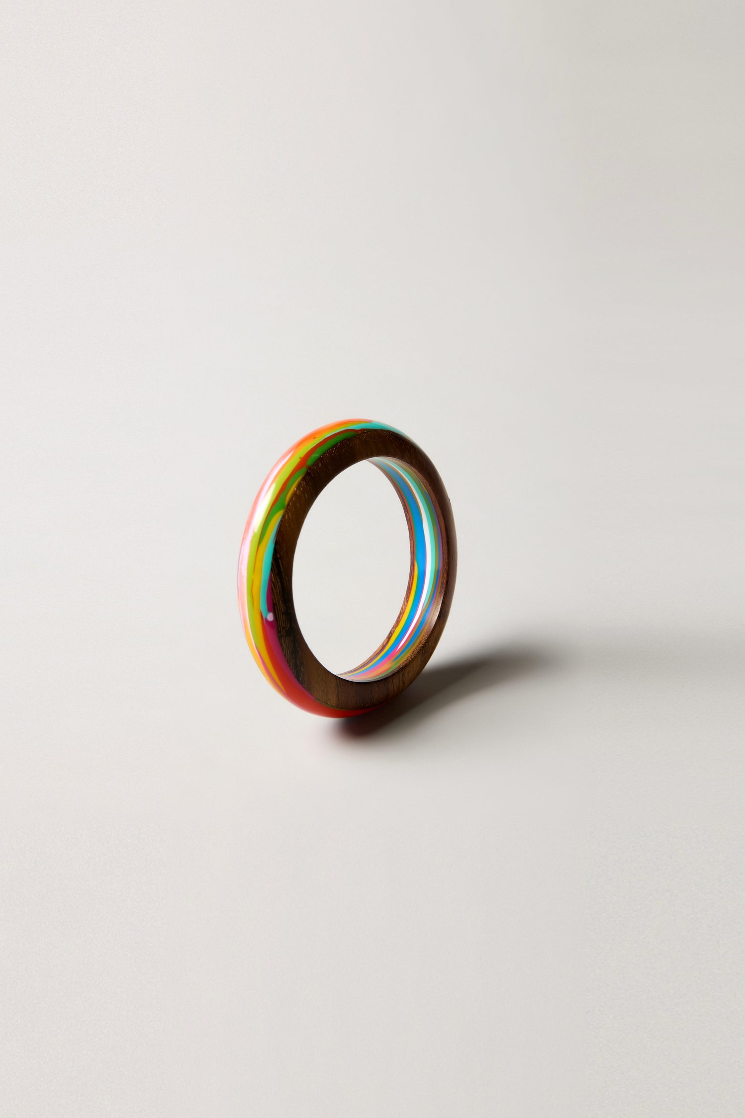 The Rainbow Marble Bangle is a multicolored, round sculptural accessory handmade in Barcelona, shown standing upright on a plain light surface with a subtle shadow.