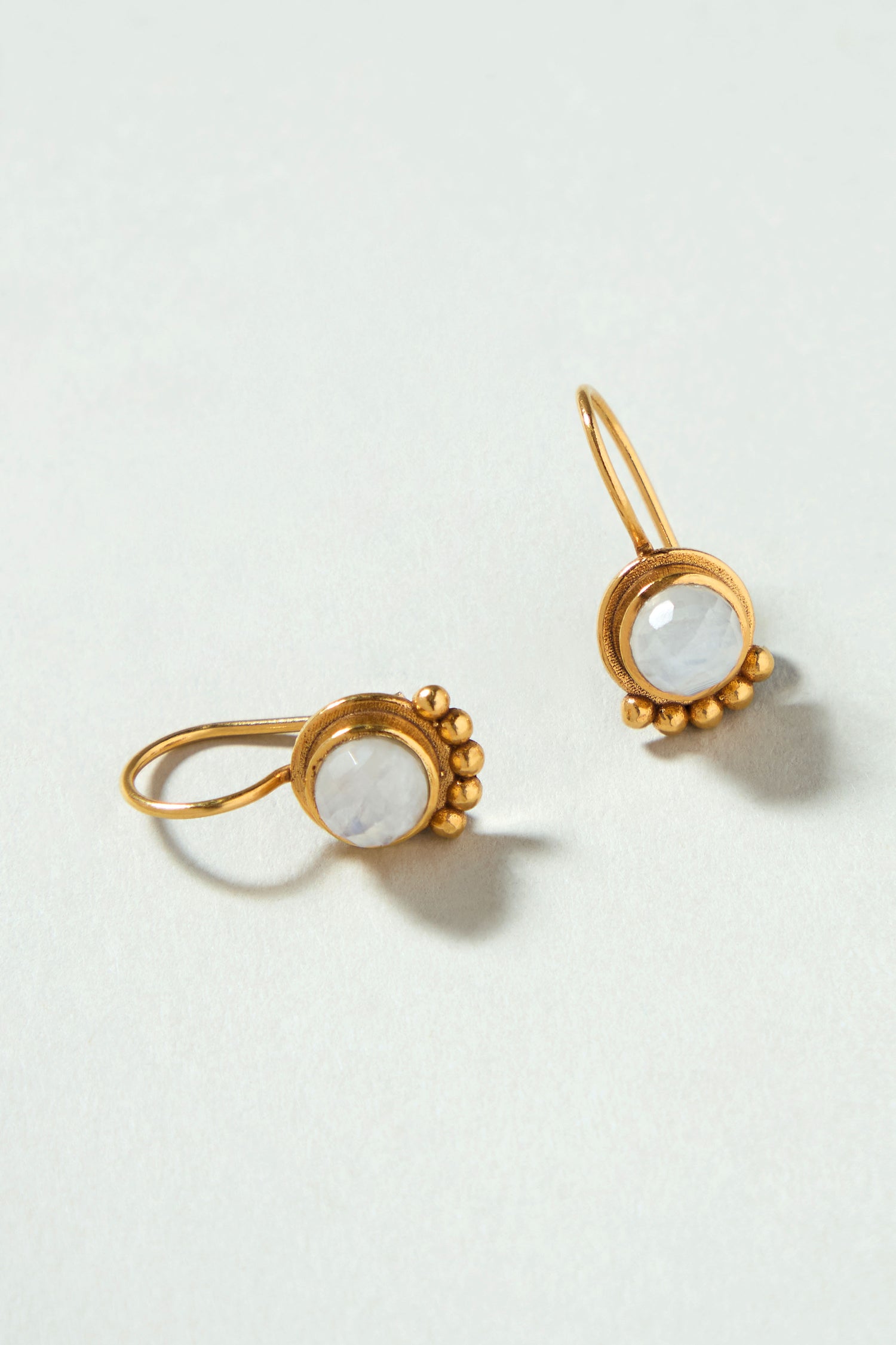 Moonstone Earrings: Gold plated earrings with round white stones and delicate bead accents, beautifully handcrafted to add a touch of elegance to any outfit. Displayed on a light surface for a refined look.