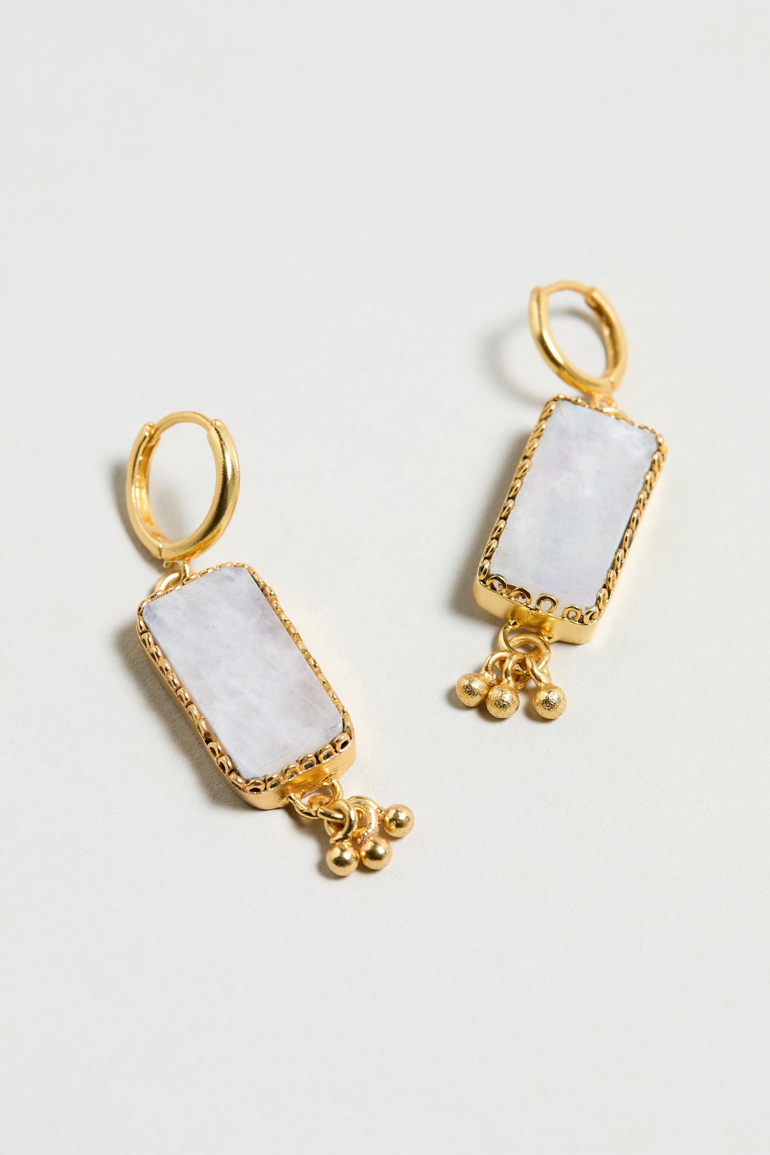Hand Crafted Rainbow Moonstone Rectangle Earrings feature gold plating, white moonstone centers, and three small gold bead dangles at the bottom, presented on a light background.