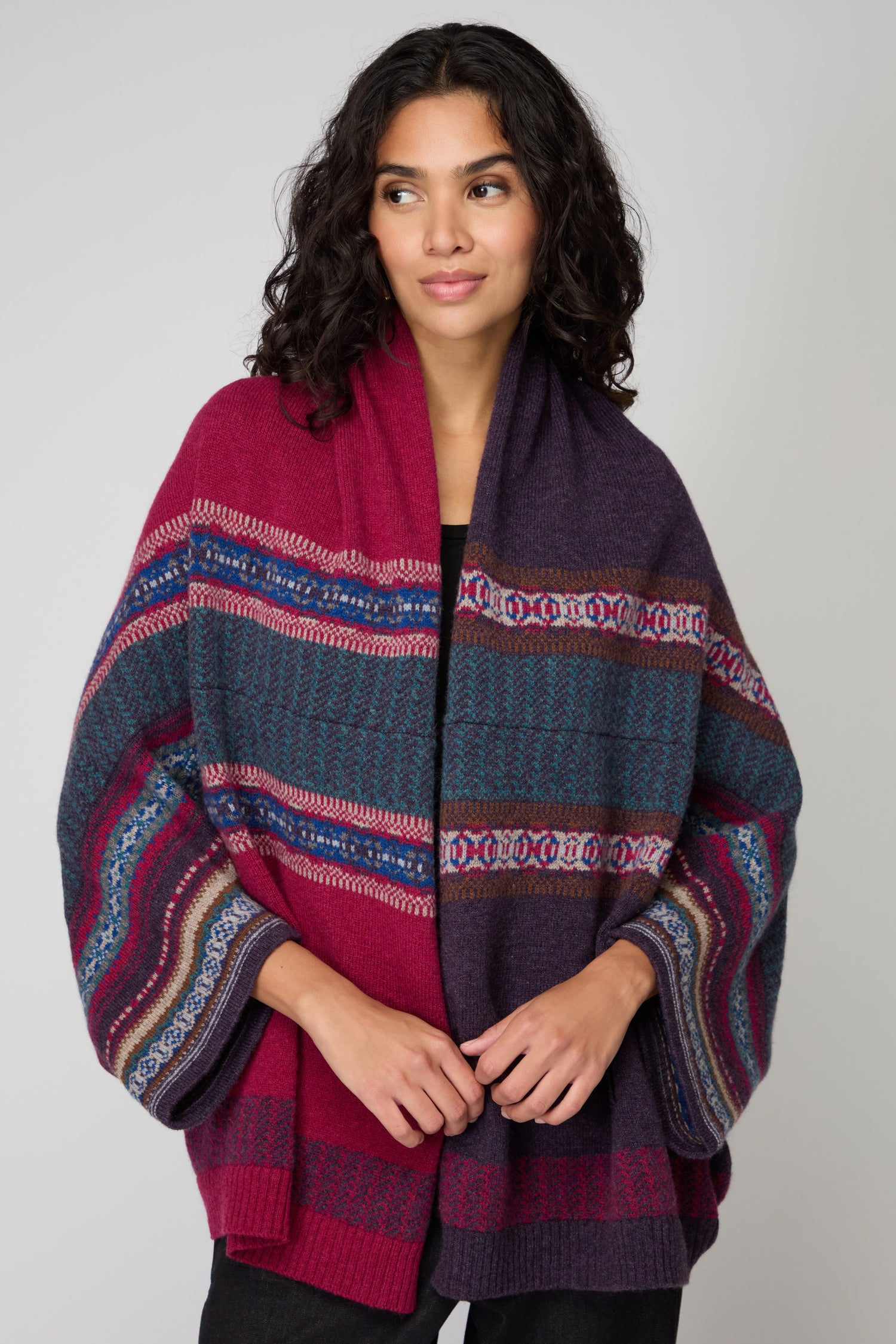 A woman wears the Bramble Montrose Blanket Cardigan, featuring a patterned design in dark and red tones, standing against a plain light background.