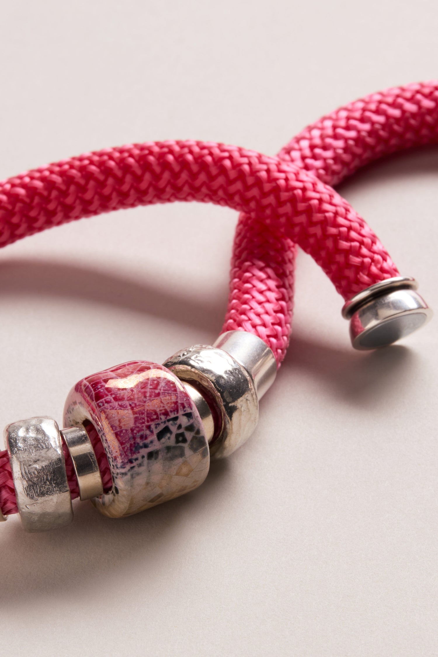 Close-up of a pink braided rope bracelet with silver and ceramic bead accents, styled alongside the Single Mosaic Cube Necklace, on a neutral background.