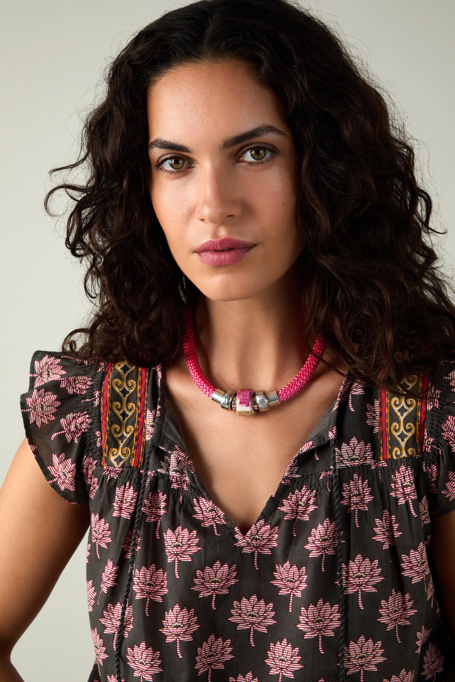 Woman with curly dark hair wears a patterned dress and the Single Mosaic Cube Necklace, standing against a plain background.