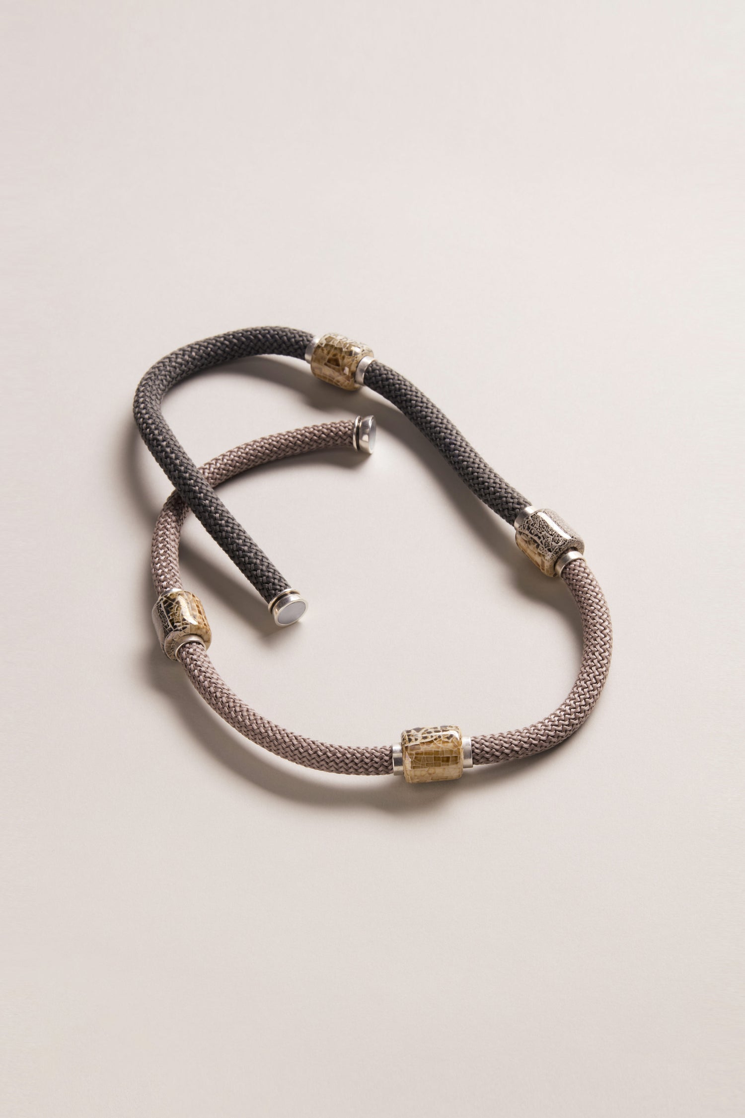 The Long Mosaic Bead Necklace features silver and gold cylindrical accents in a two-tone design inspired by Mediterranean jewelry, displayed on a neutral background.