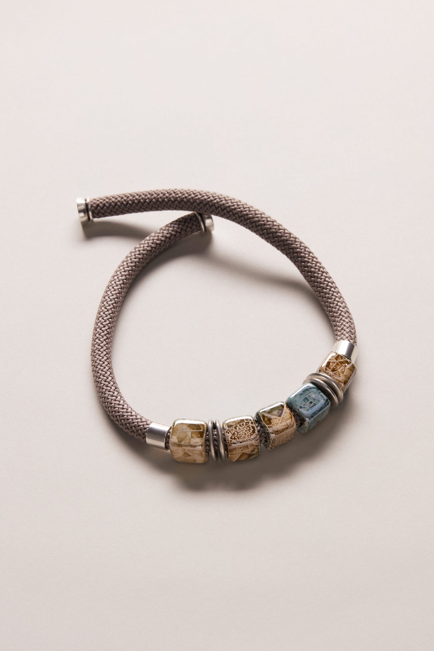 A braided taupe bracelet with silver end caps and five earthy-toned ceramic beads, perfect to pair with your Short Marble Cube Necklace or other taupe and teal jewelry.