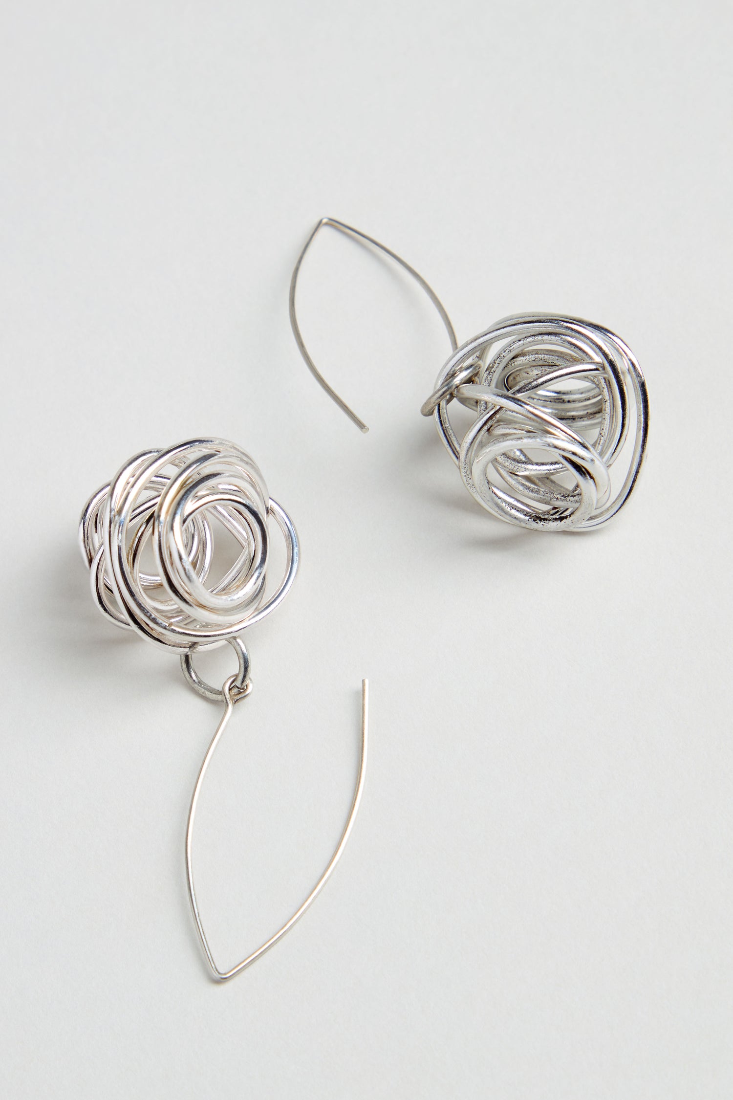 The Silver Scribble Earrings feature a unique tangled knot design with curved, thin wire hooks for a sculptural look that’s lightweight and stylish.