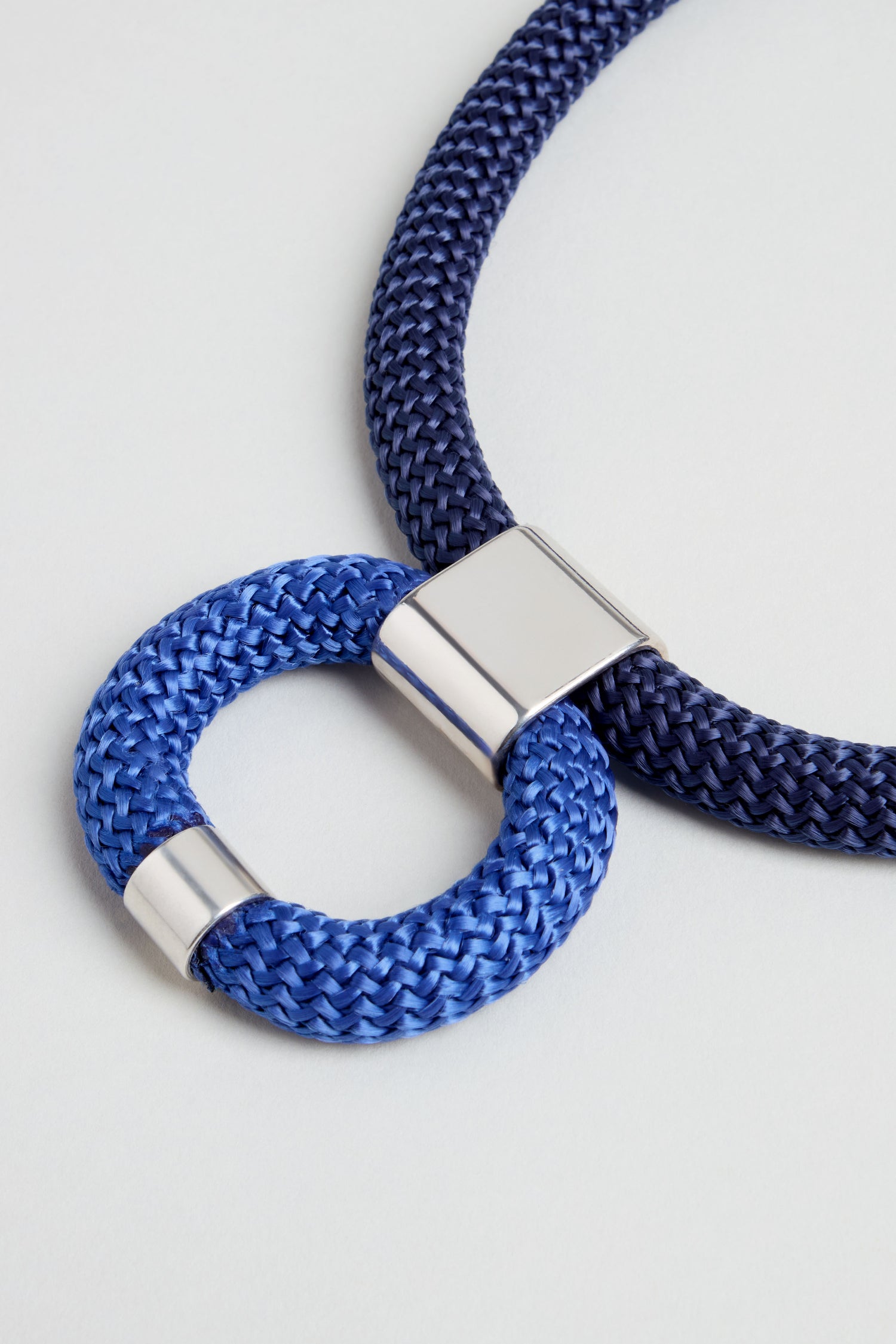 The Navy Cord Hoop Necklace features braided navy blue cords with metallic silver connectors and a bold circular hoop pendant—perfect as a statement accessory.