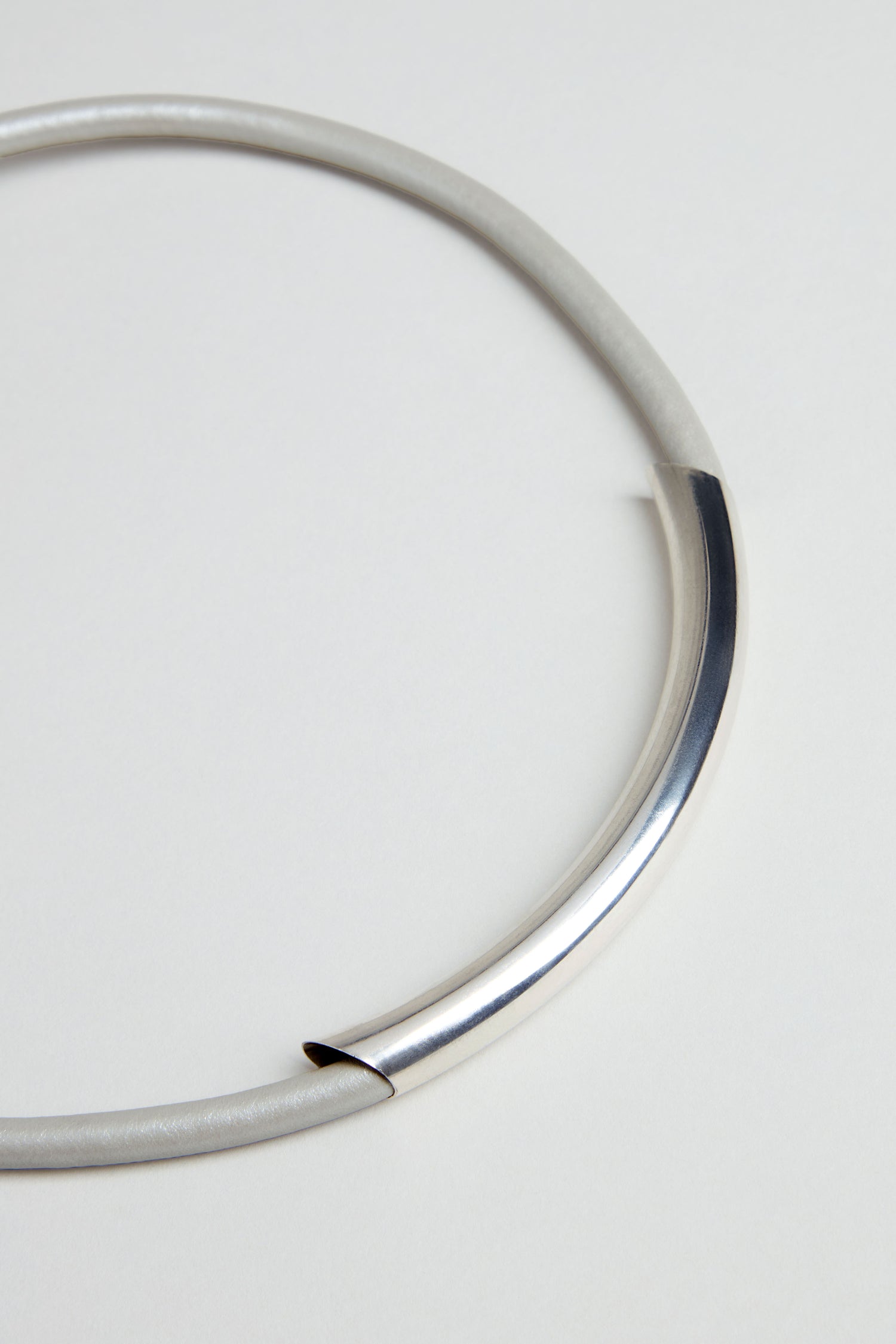 The Grey Leather Cord Necklace features a silver cylinder accent on a smooth, curved band, offering modern minimalist style and understated elegance—an ideal piece to elevate any look.