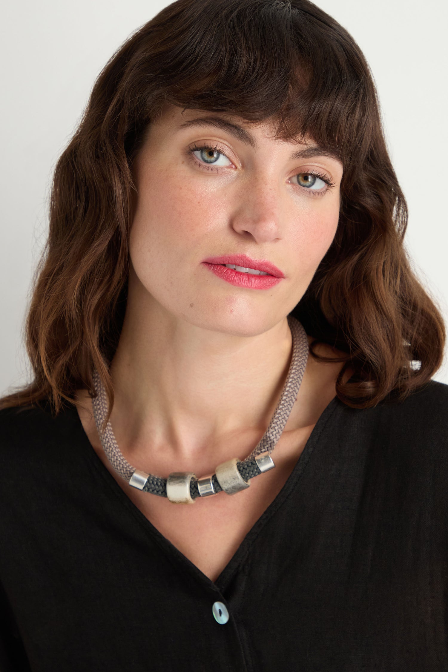 Woman with wavy brown hair wearing a black top and the Layered Marble Bead Cord Necklace, featuring chunky marble-effect beads, looking at the camera with a neutral expression.