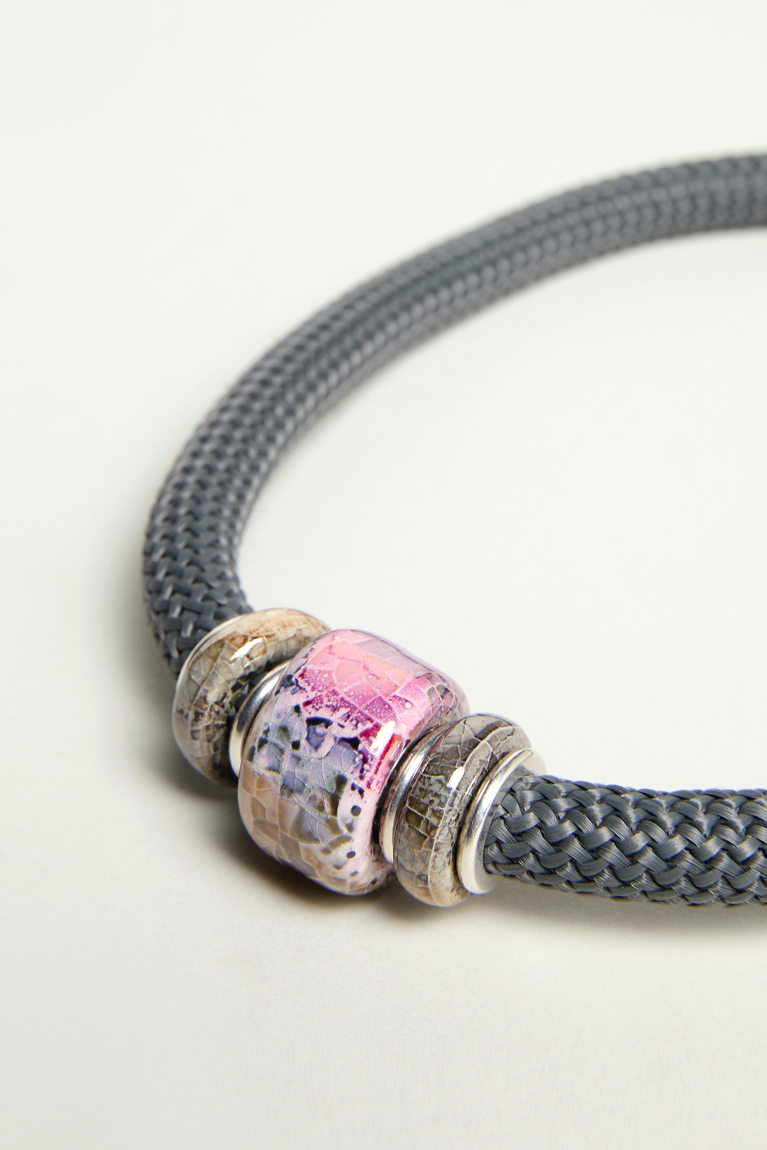 A close-up of the Pink Marble Bead Short Cord Necklace, a handmade statement piece with three round, patterned beads in pink, beige, and silver on a chunky cord.
