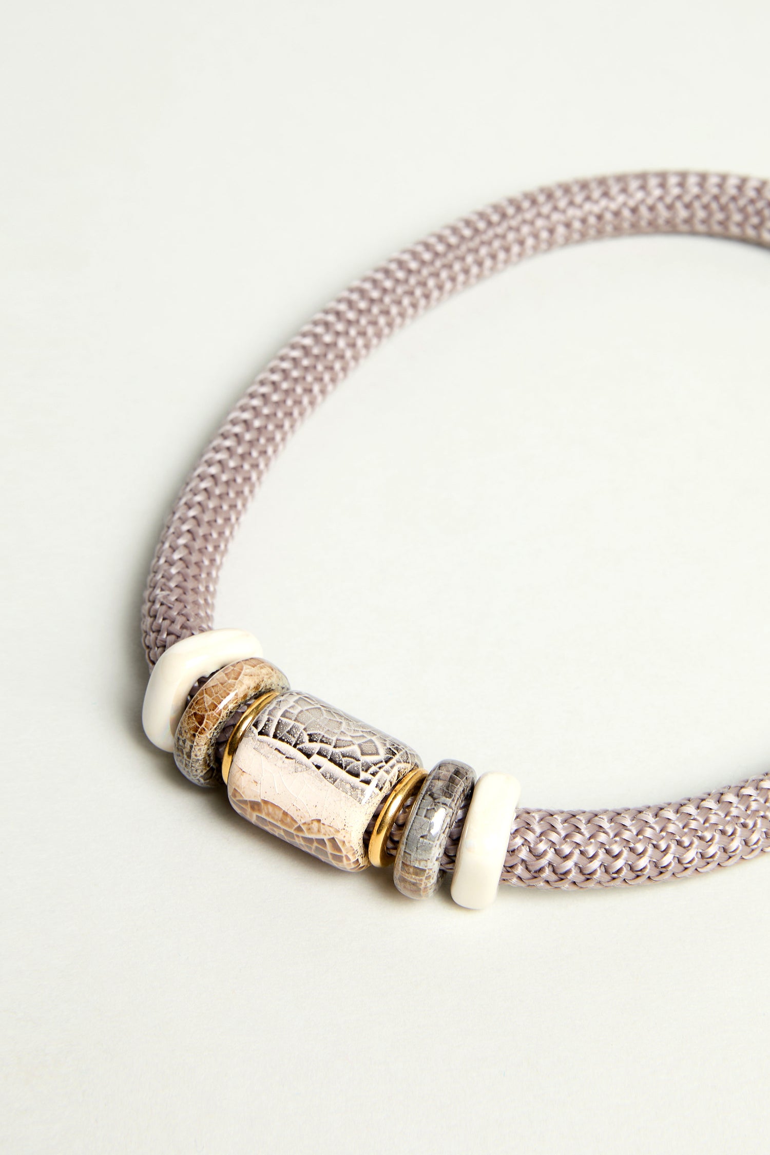The Mosaic Marble Bead Short Cord Necklace is a braided lilac cord featuring three cylindrical, textured metal and ivory-colored beads at the center—a Sahara Exclusive that adds a unique touch to any style.