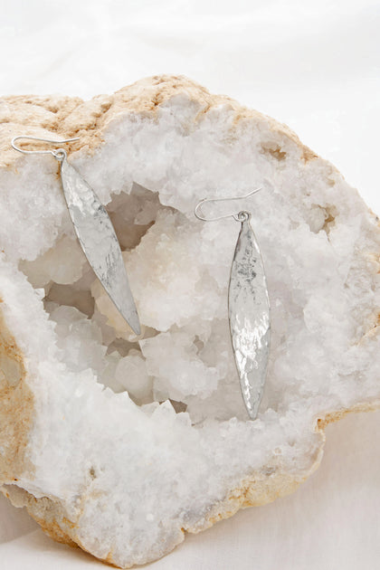 The Hammered Silver Leaf Earrings from Etnika elegantly drape across a rough white crystal cluster.