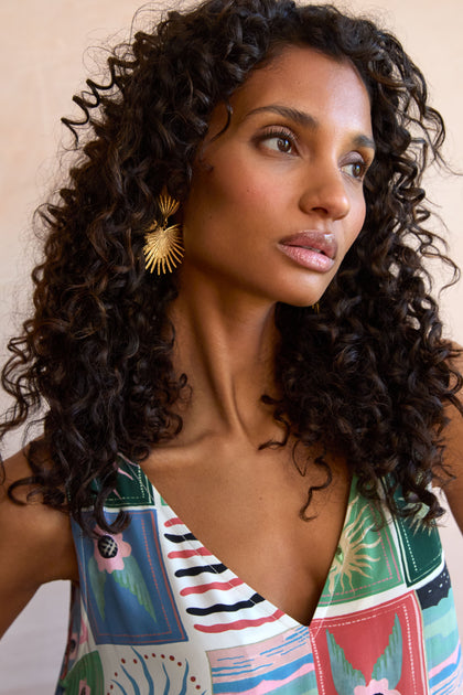 A woman with curly hair wears a patterned sleeveless top from EUNELECTRA-AW25 and Gold Plated Stargazer Earrings, looking slightly to the side.