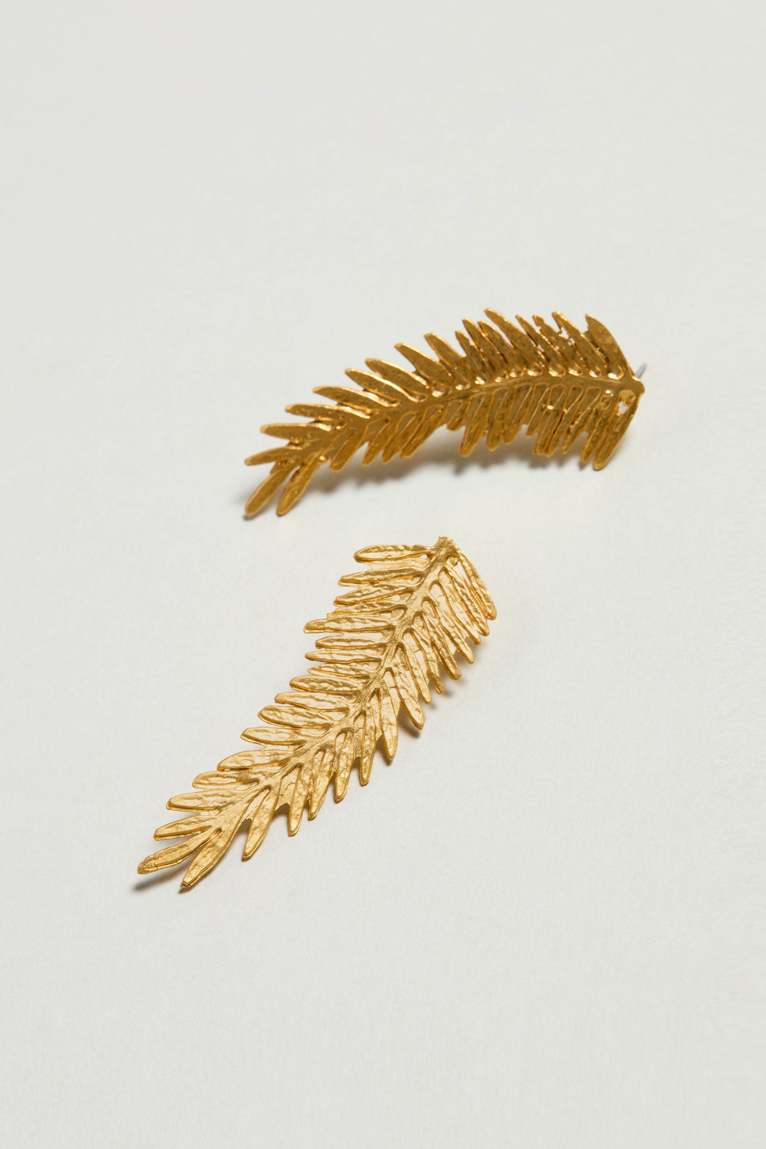 A pair of gold plated feather earrings are displayed on a plain white surface.
