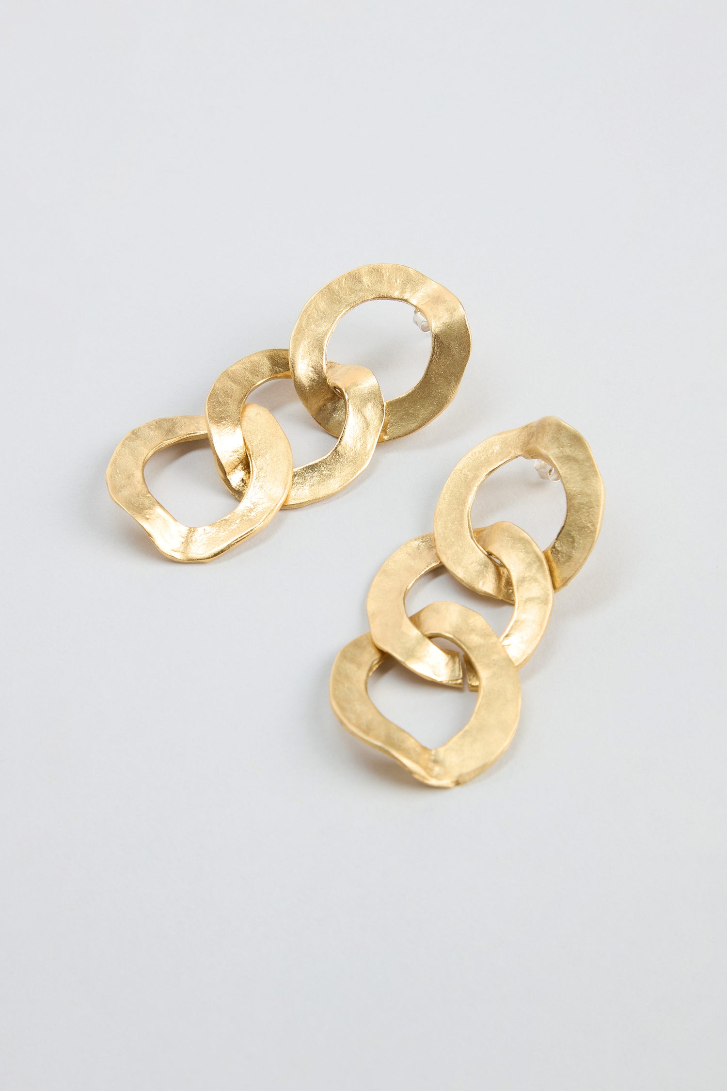 Gold Triple Hoop Earrings featuring three interlocking, textured circular links in a gold-tone statement drop design, displayed on a light gray background.