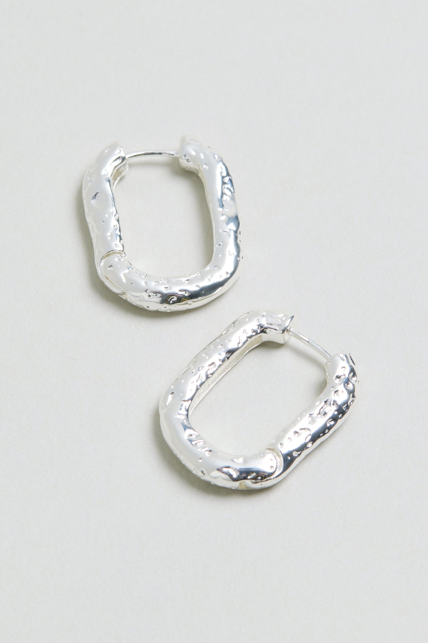 Introducing the Hammered Hoop Earrings: a pair of chunky, textured silver hoops with an irregular, rectangular silhouette—reminiscent of hammered metal—presented against a light background.
