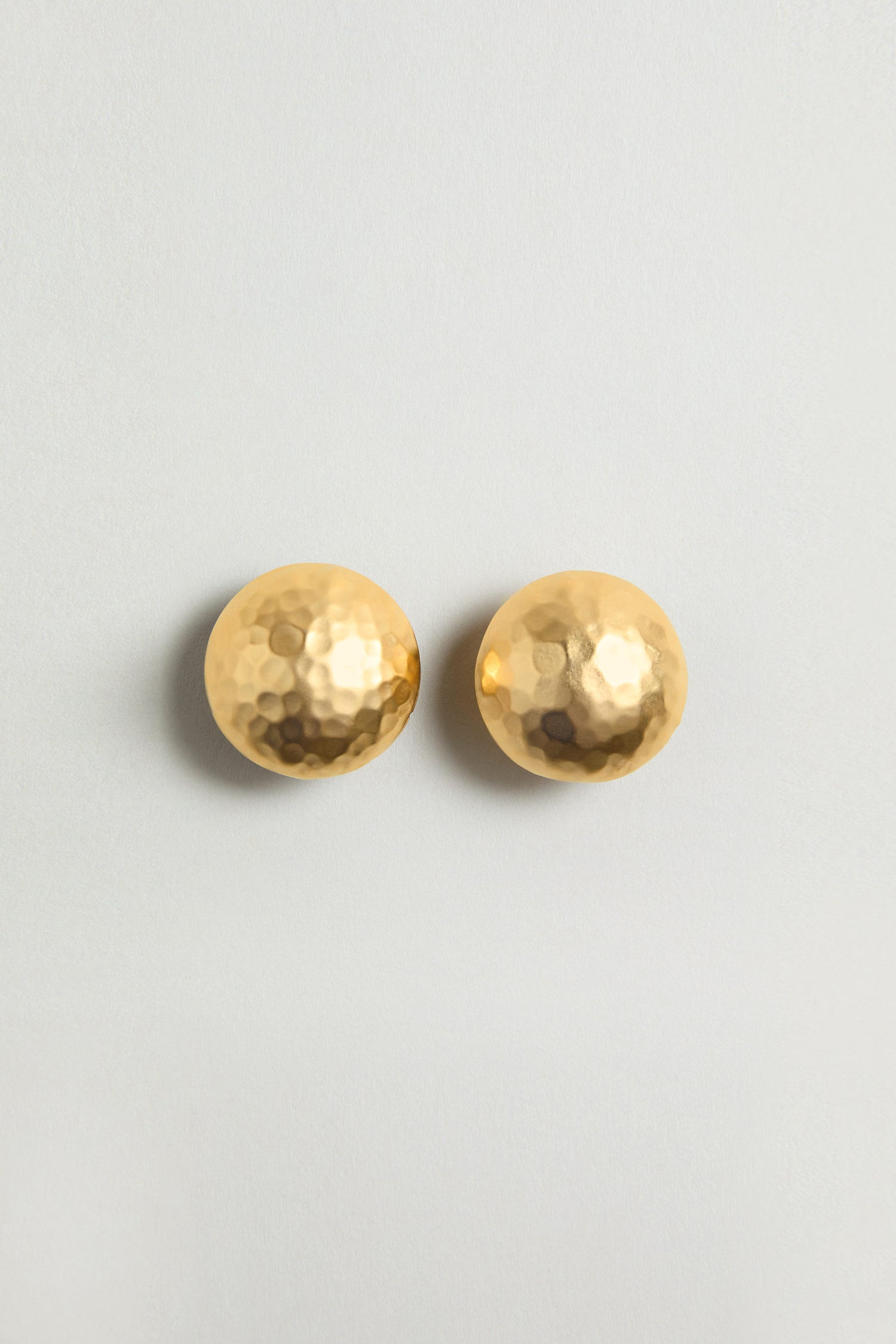 The Gold Plated Hammered Sphere Earrings, featuring a round, textured design, are displayed on a plain light background and add elegant style to any outfit.