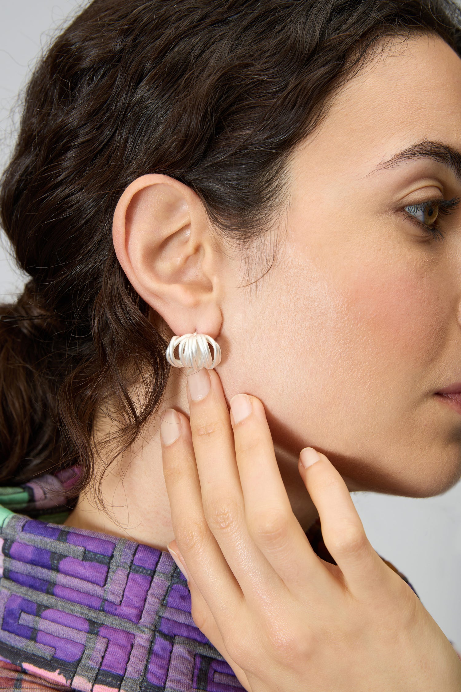 A woman with dark hair touches a Silver Vortex Earring on her left ear. She wears a colorful, patterned top in shades of purple.